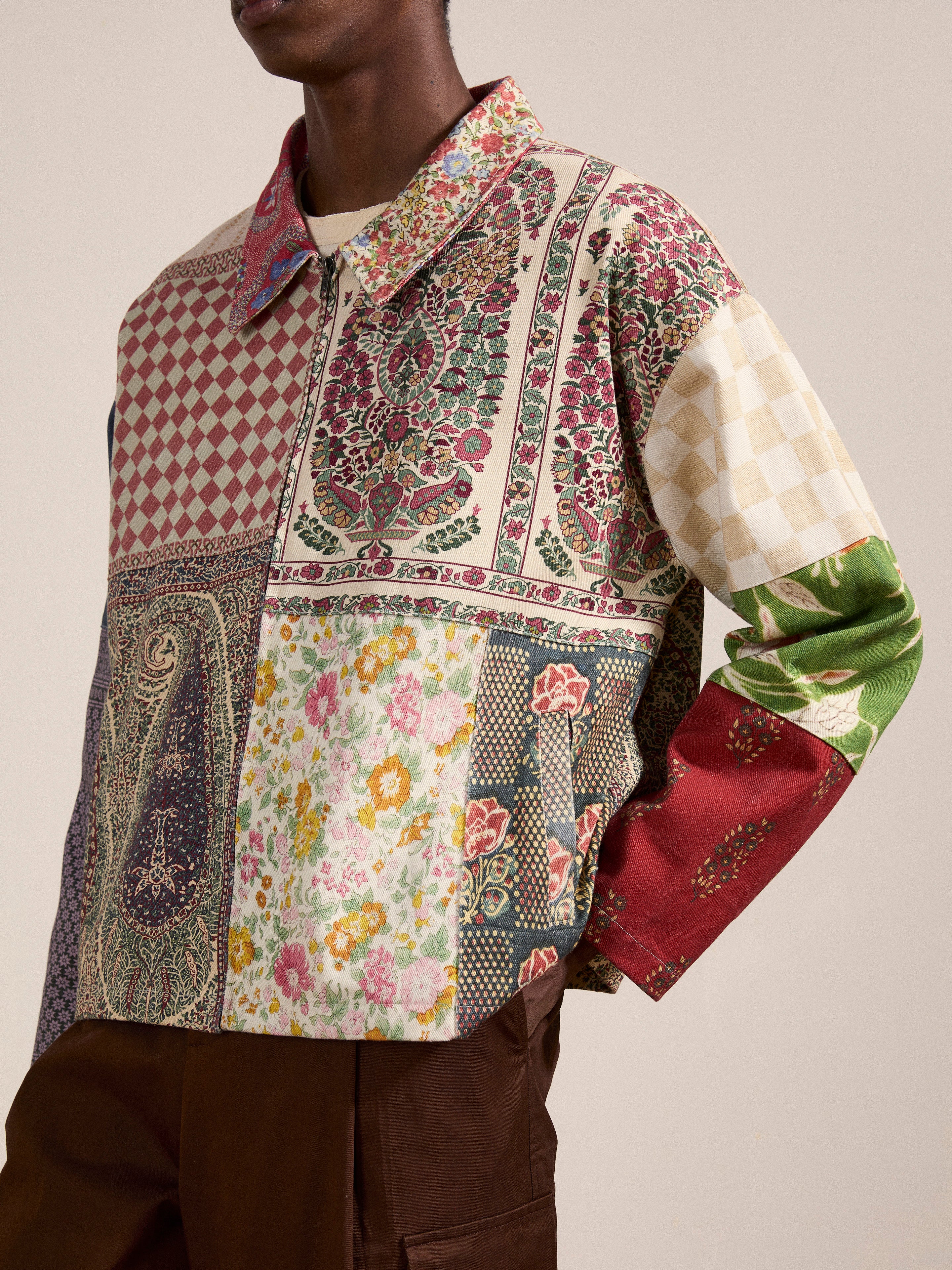 Person wearing a multicolored Tapestry Twill Jacket by FOUND, featuring various South Asian patterns, standing against a plain background.