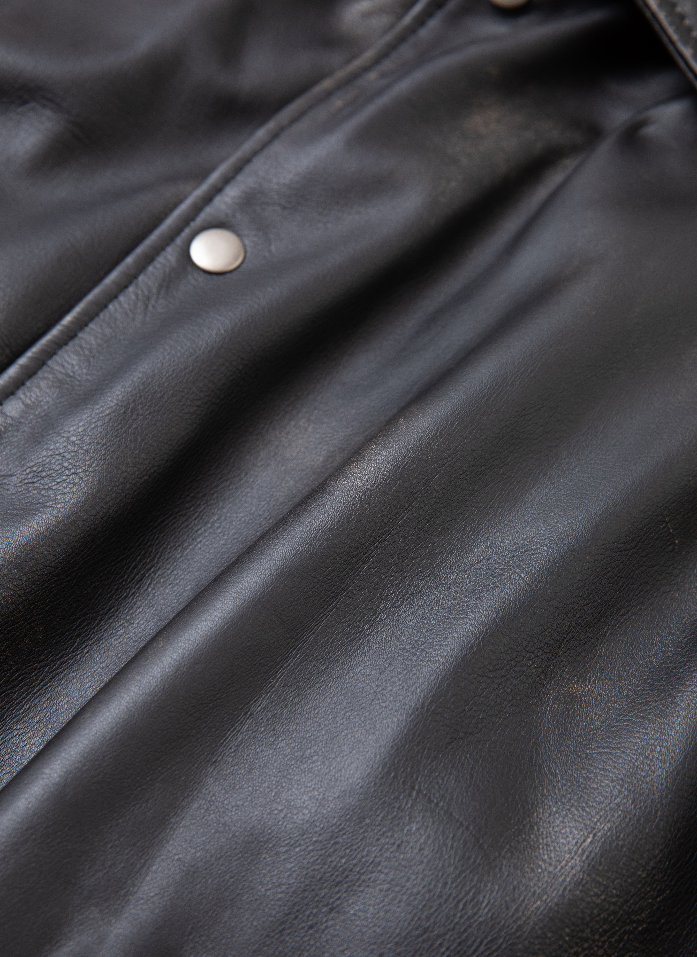 Close-up of the FOUND Logan Distressed Leather Varsity Jacket featuring silver buttons. The texture of the genuine hand-distressed leather is visible, showcasing its smooth and slightly worn surface, complemented by a rich satin lining.