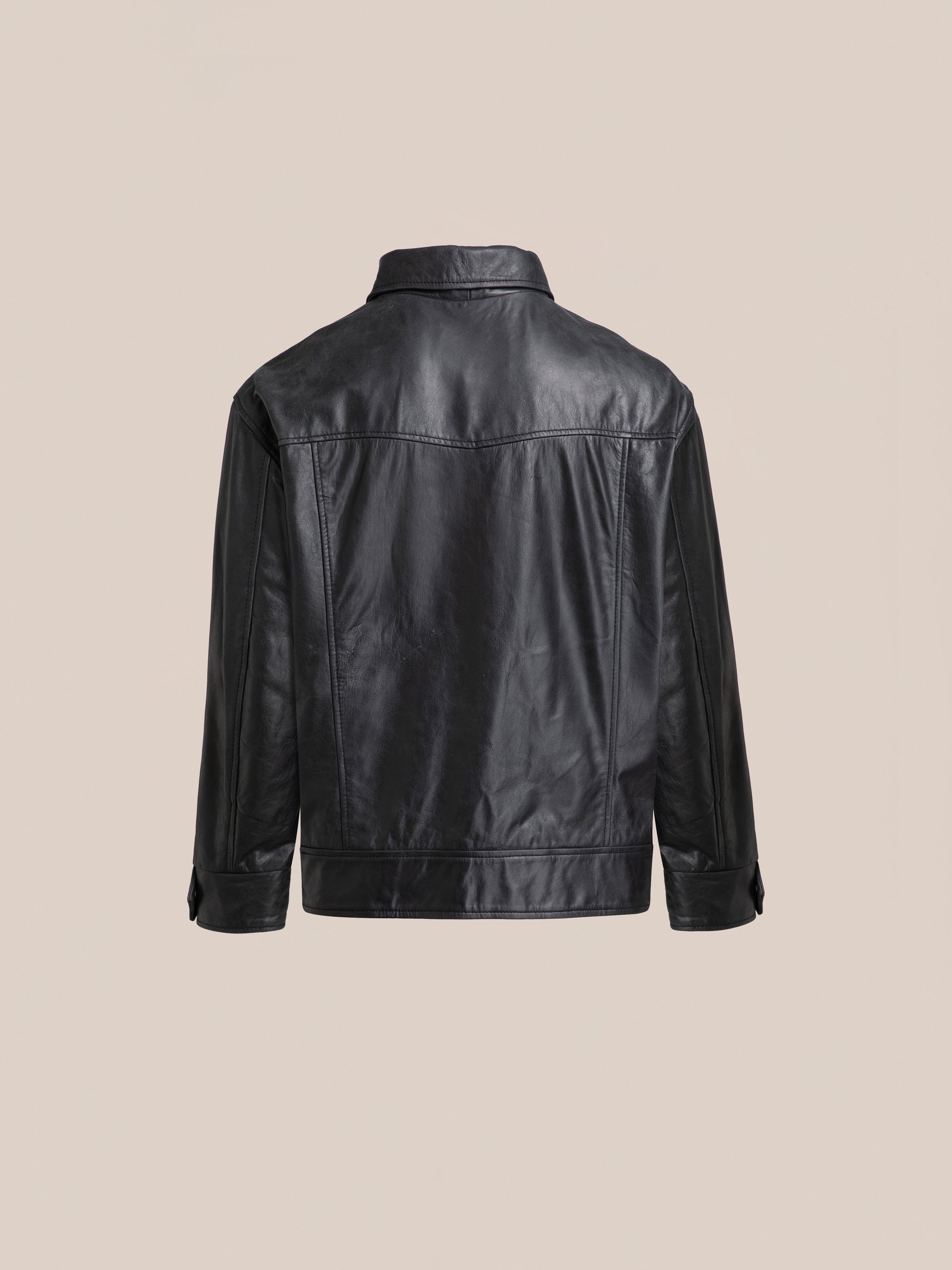 Back view of the Leather Trucker Jacket by FOUND, featuring long sleeves and a collar in black leather, set against a plain beige background.