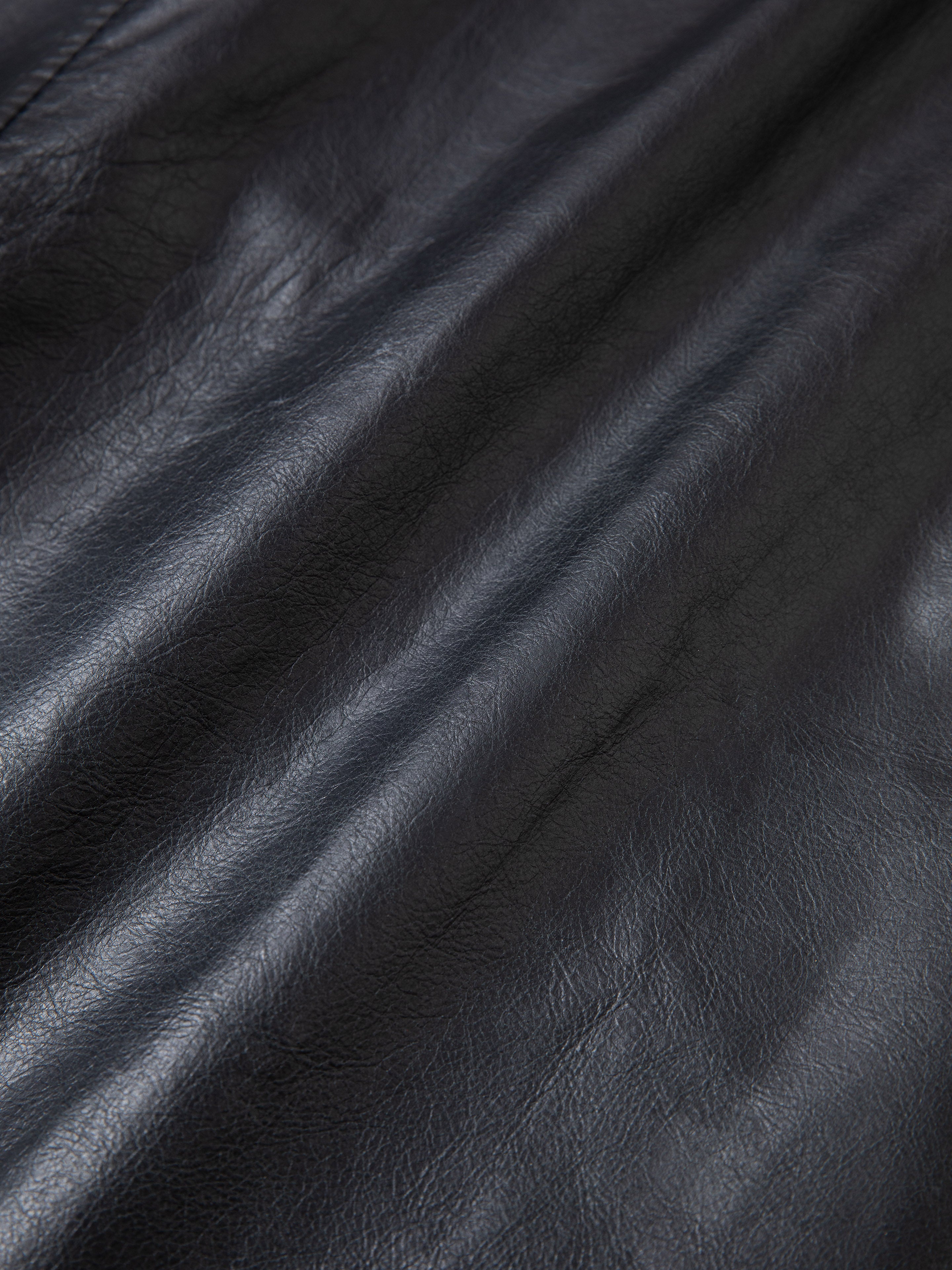 Close-up of a folded piece of black leather with visible texture and grain, reminiscent of the sturdy material used in a FOUND Leather Trucker Jacket.