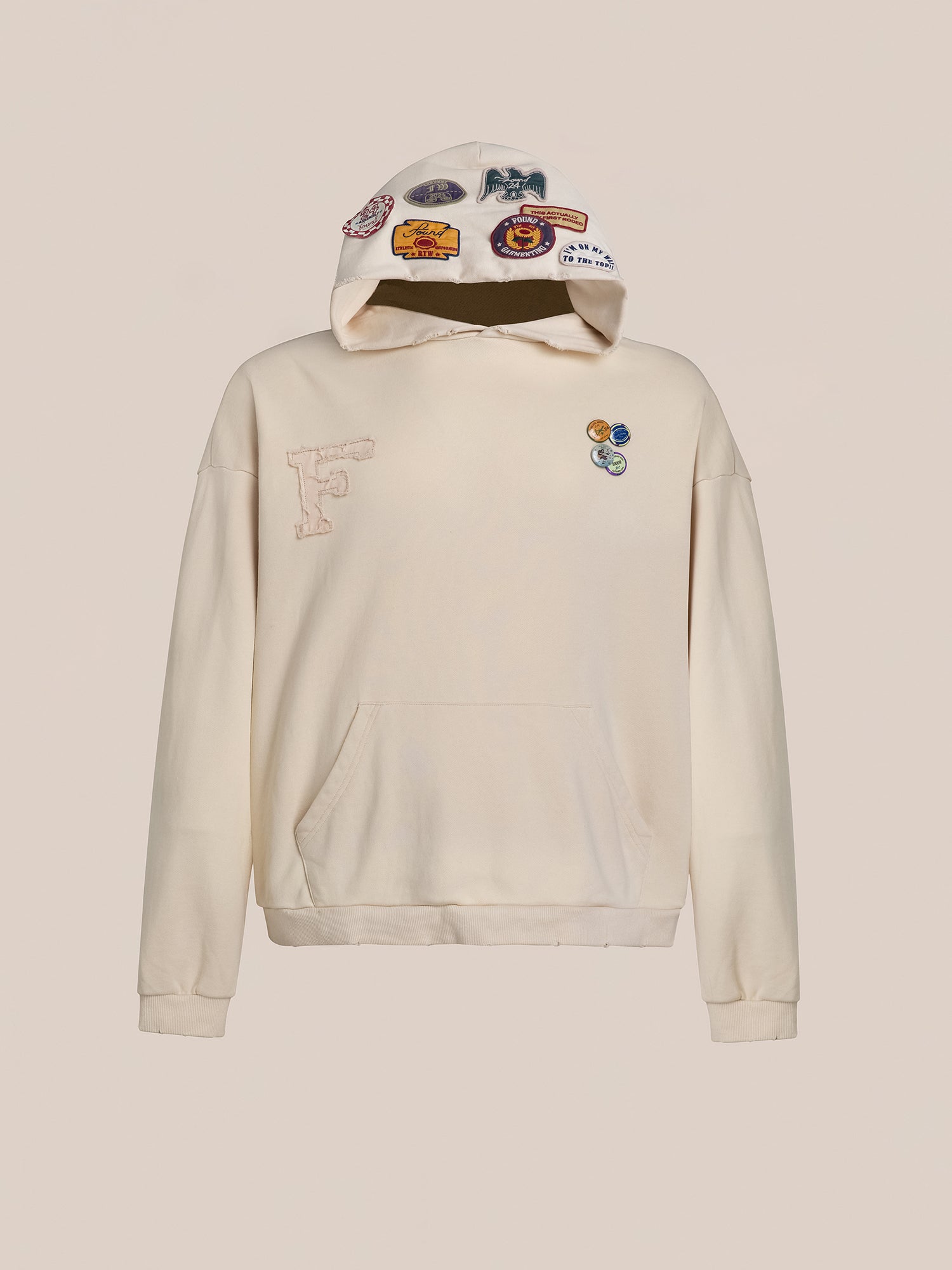 The Faded Patch Hoodie by FOUND features a vintage aesthetic with its off-white coloration and vibrant patches adorning the hood and chest, complemented by a spacious front pocket. Its oversized fit ensures added comfort and a relaxed style to enhance any ensemble.