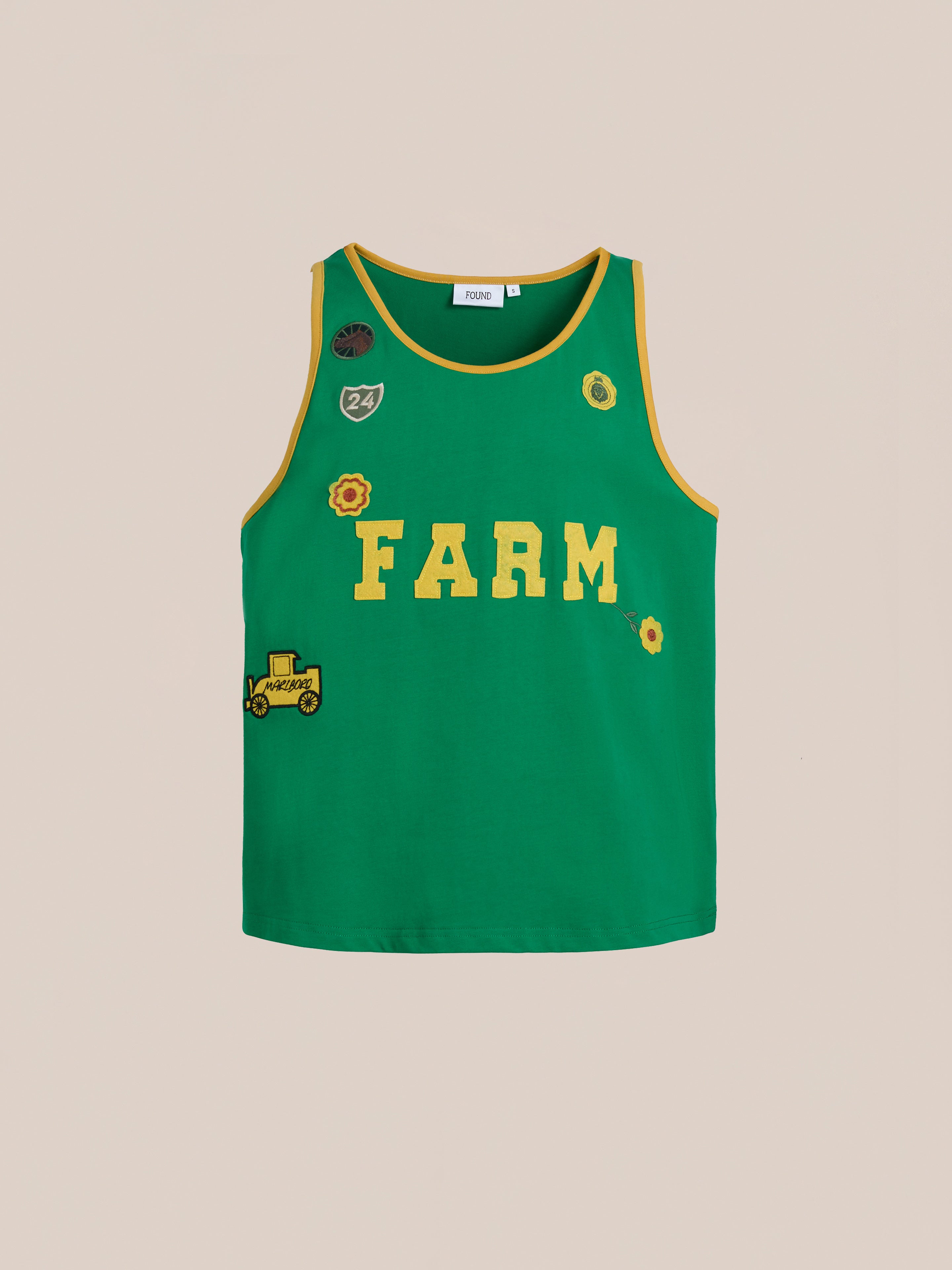 The Farm Tank by FOUND is a green sleeveless top with yellow trim, vintage athletic "FARM" text, and embroidered patches of a flower, tractor, and number 24 on light beige. Made from breathable cotton for comfort.