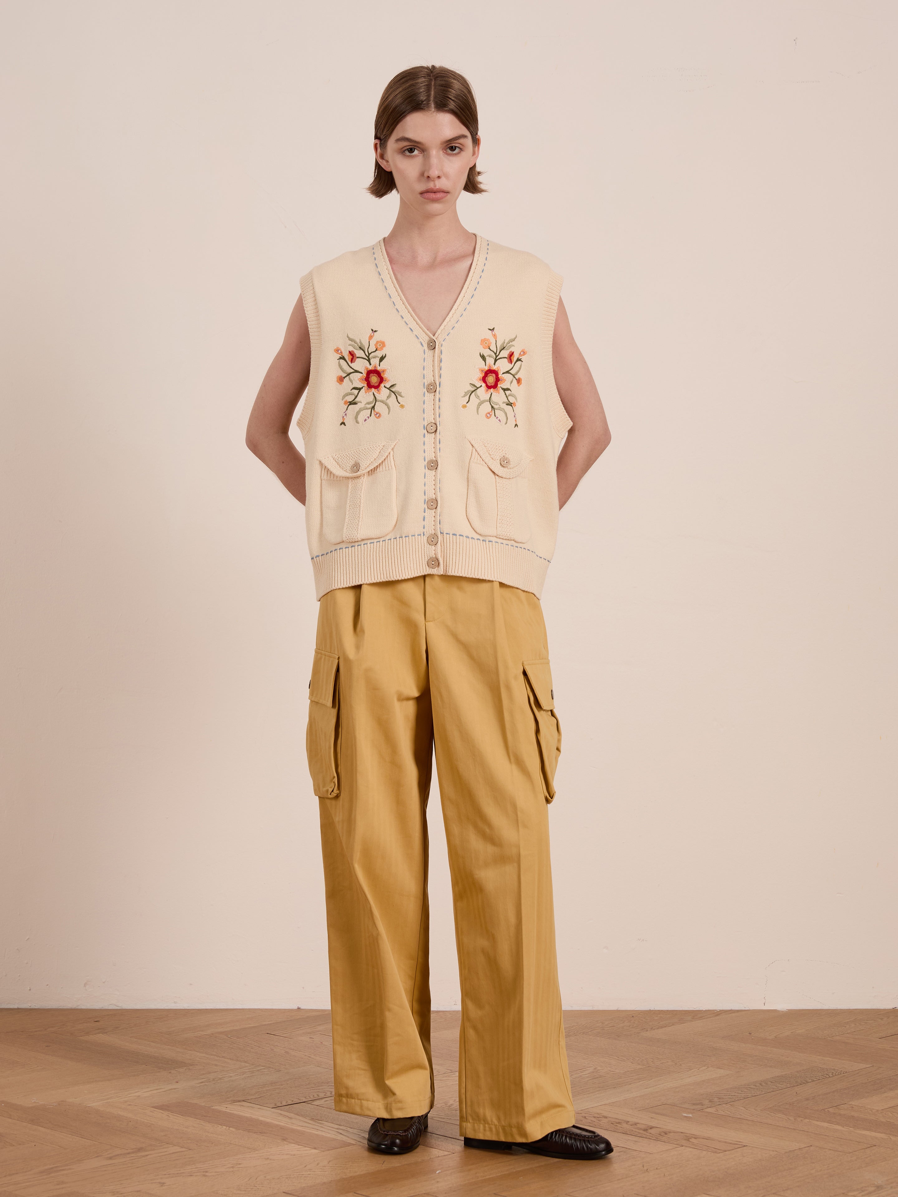 A person stands against a plain background wearing the FOUND Floral Embroidered Knit Vest, paired with yellow cargo pants.