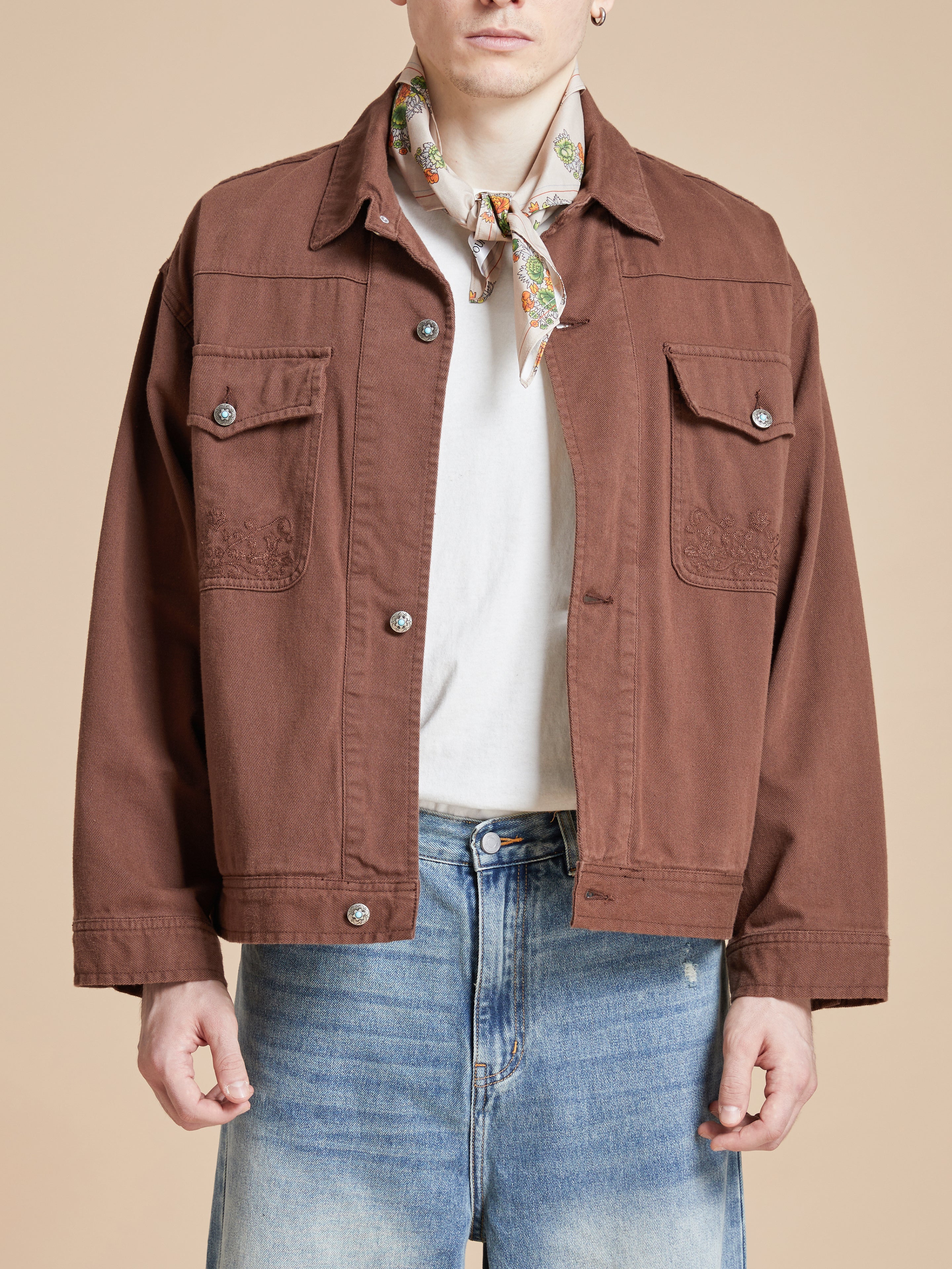 A man wearing a brown jacket and jeans with motifs inspired by nature. He happens to be sporting the Found Floral Print Bandana.