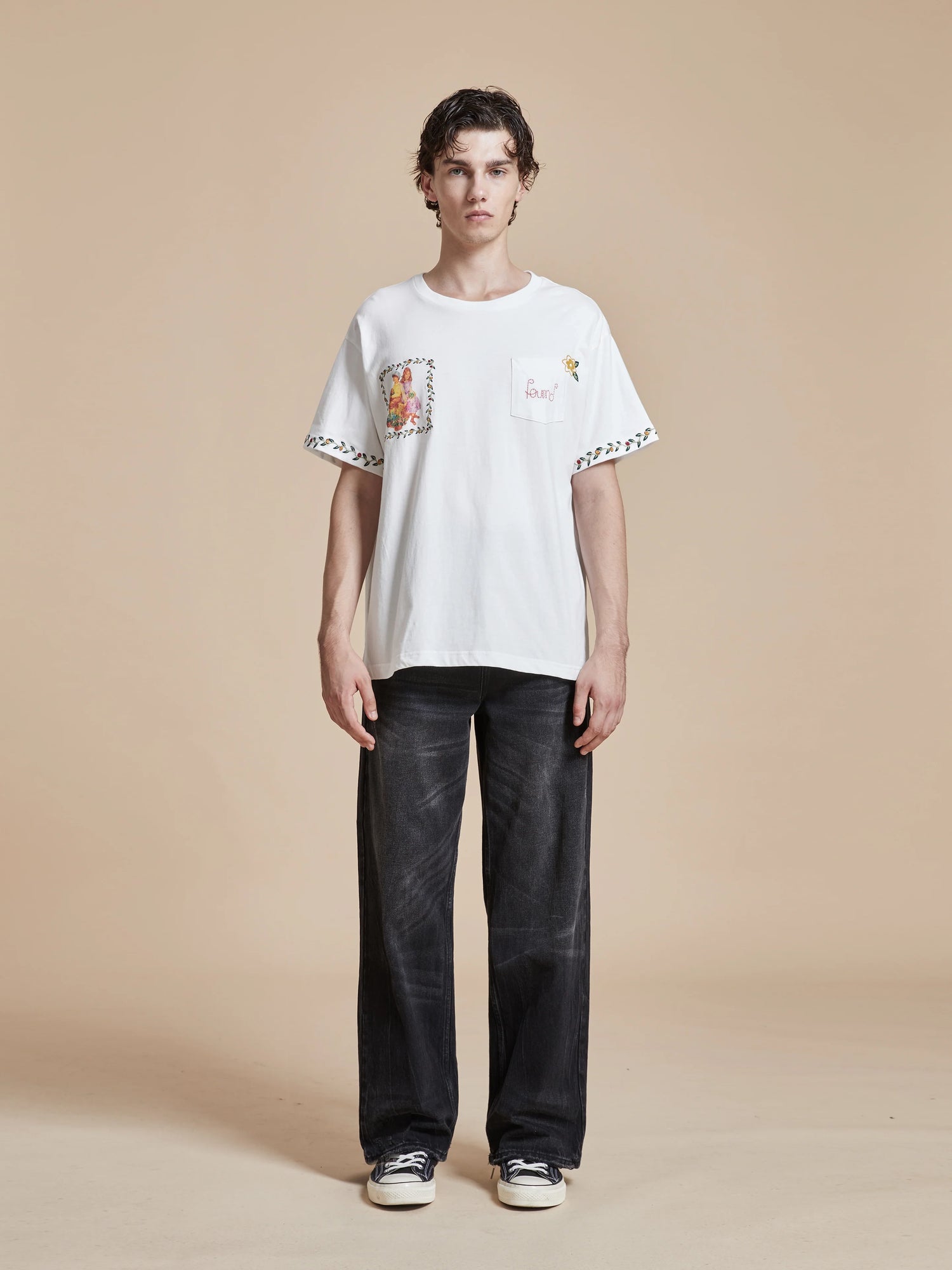 A man wearing a white Flower Children Tee with floral Phulkari style embroideries and black pants. Brand: Found