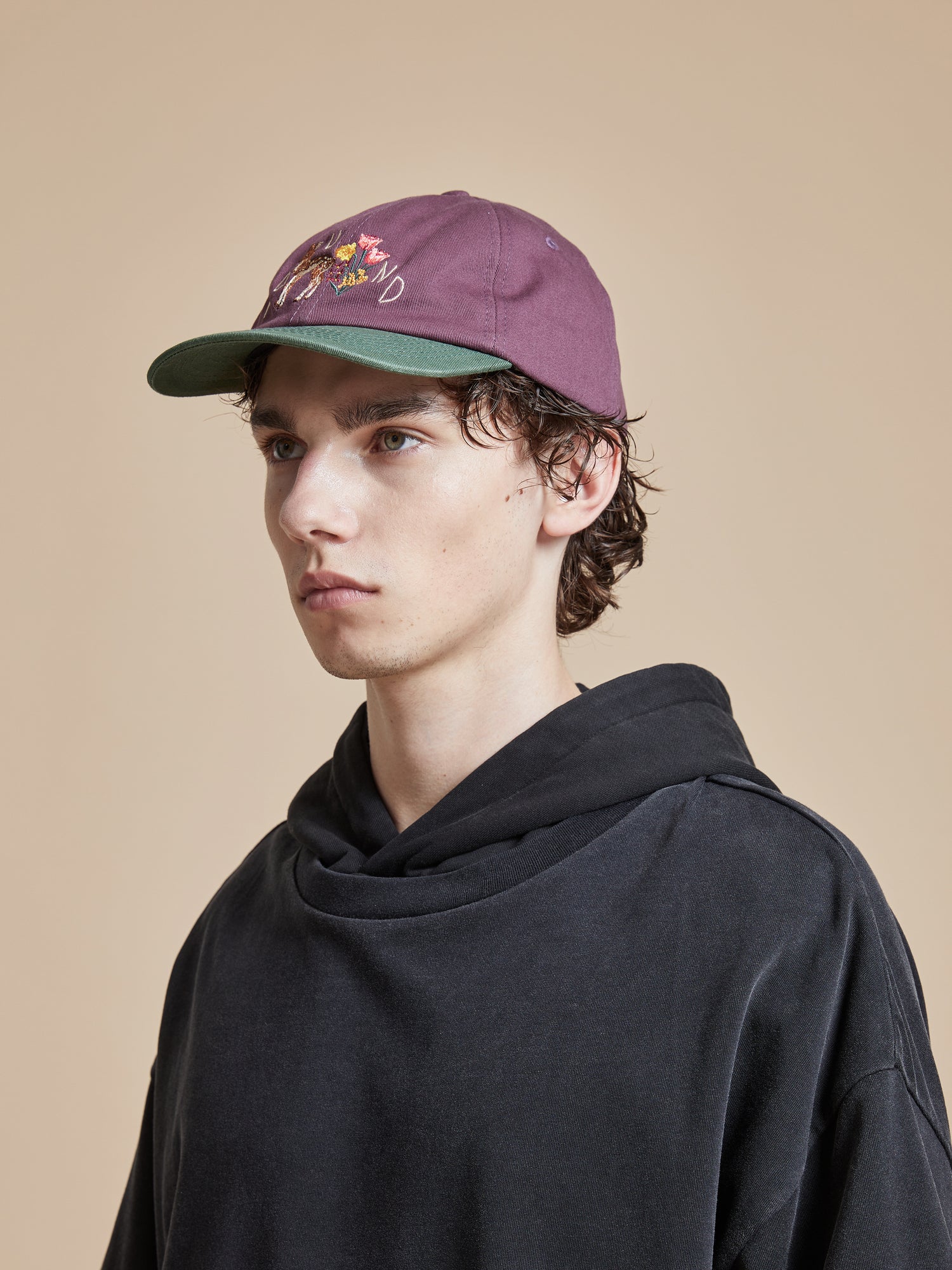 A young man wearing a black hoodie and a Found Flower Deer Cap.