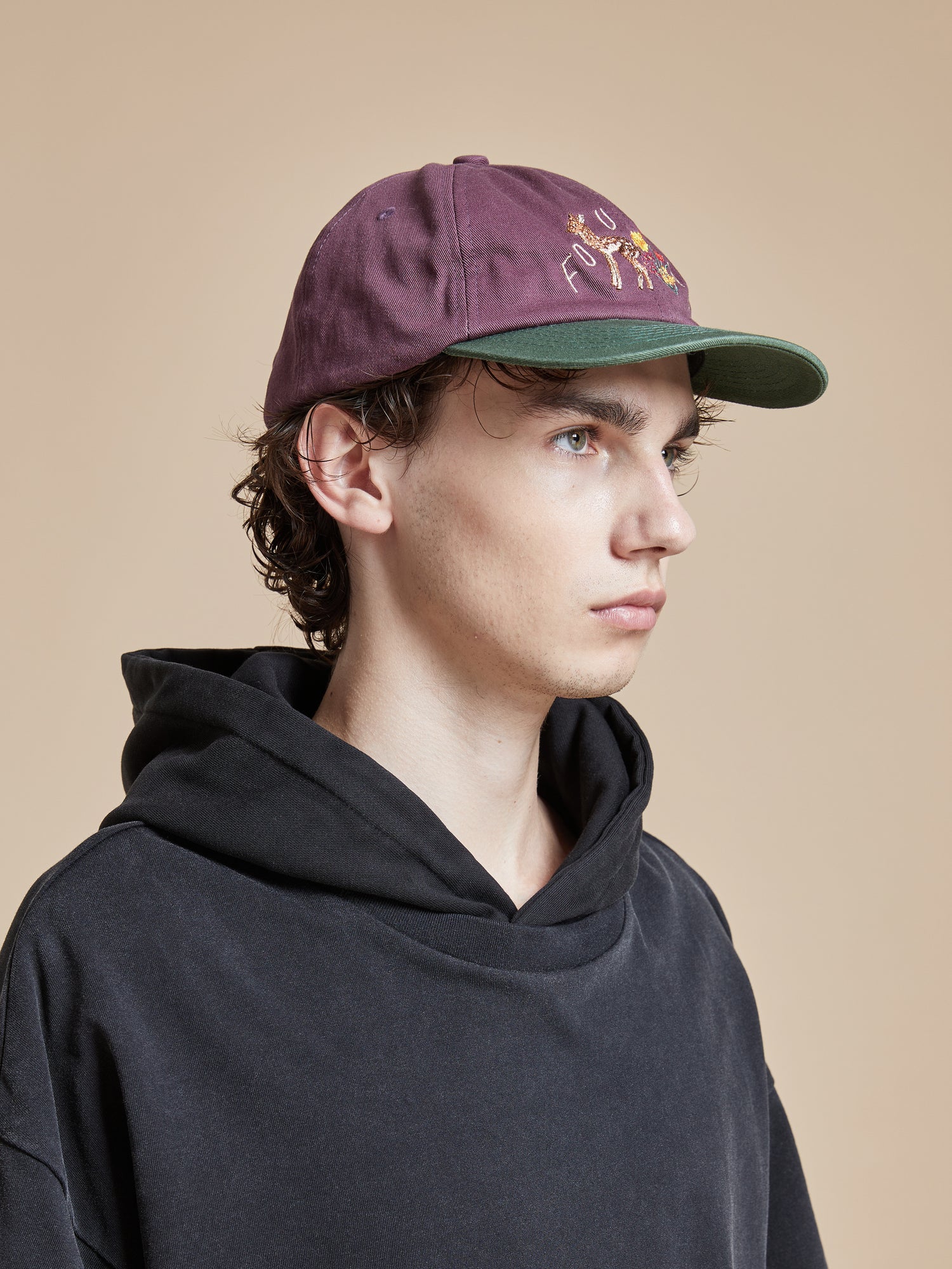 A young man wearing a Found Flower Deer Cap and black hoodie.