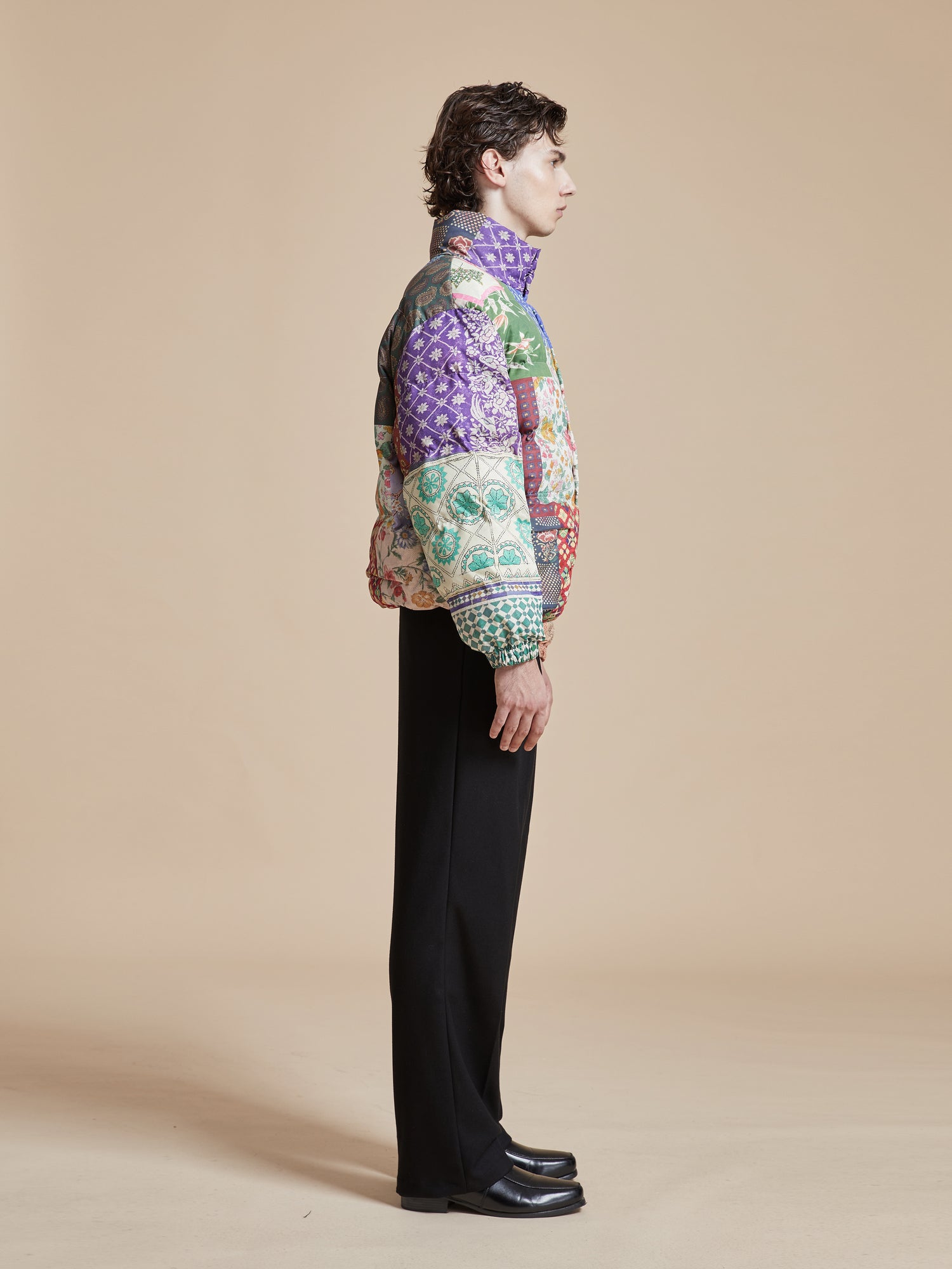 A man wearing a Gardenia Tapestry Puffer Jacket by Found featuring traditional South Asian prints.