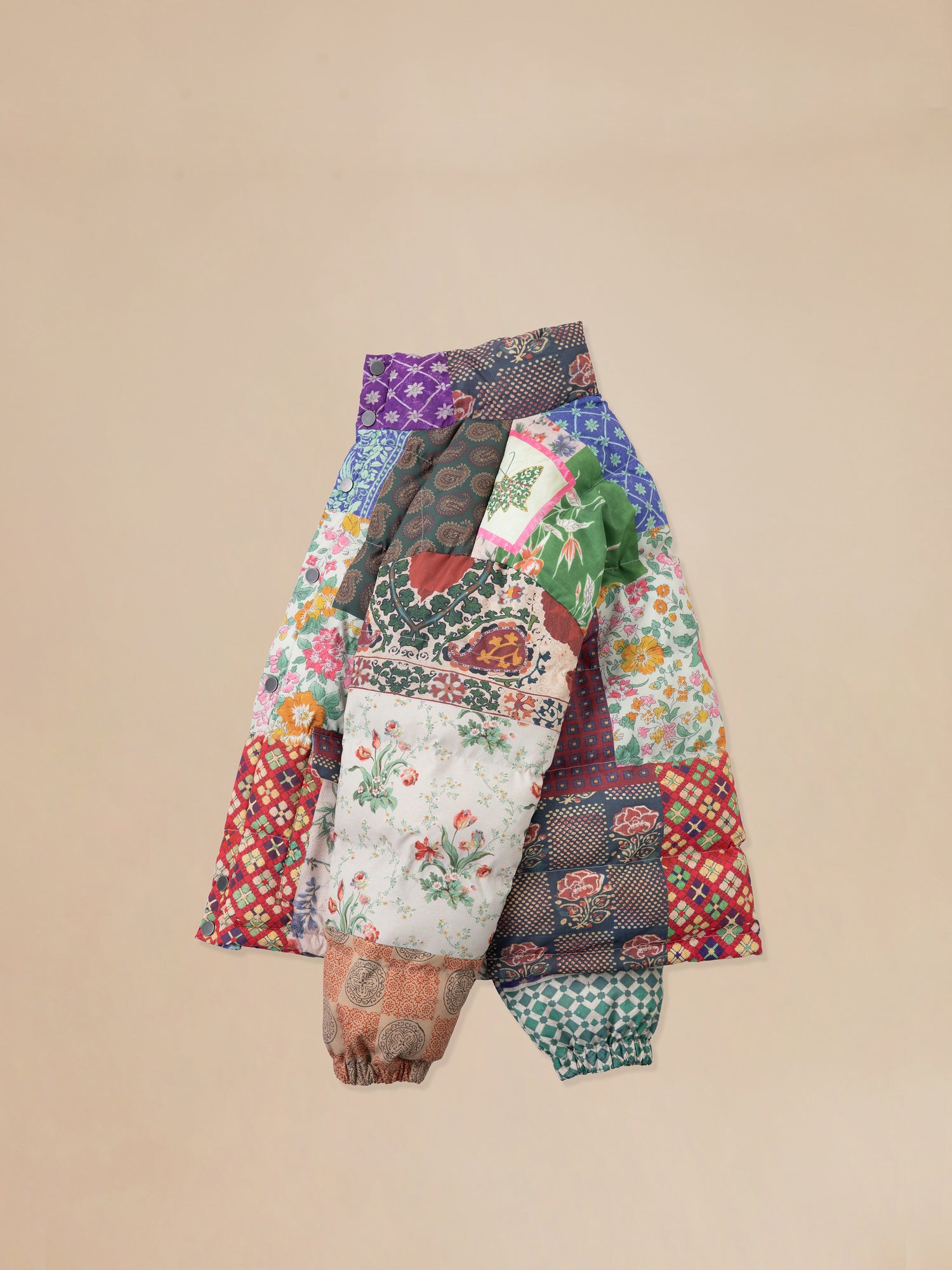 A Gardenia Tapestry Puffer Jacket featuring traditional South Asian prints on a beige background. (Brand: Found)