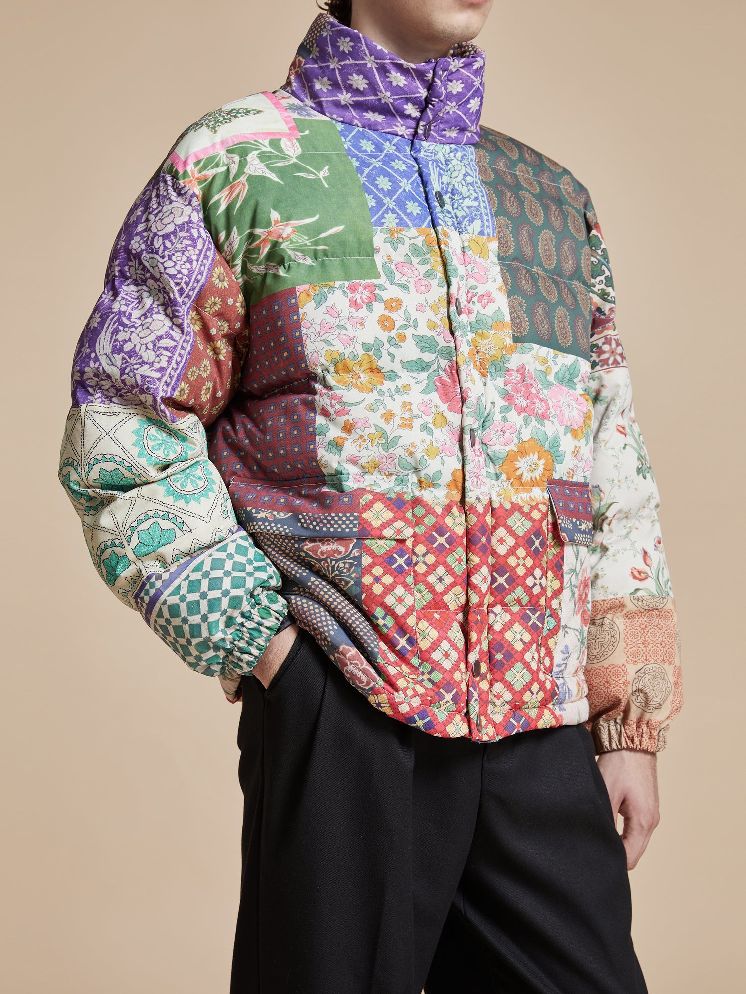 A man wearing a Gardenia Tapestry Puffer Jacket by Found, colorful traditional South Asian prints.