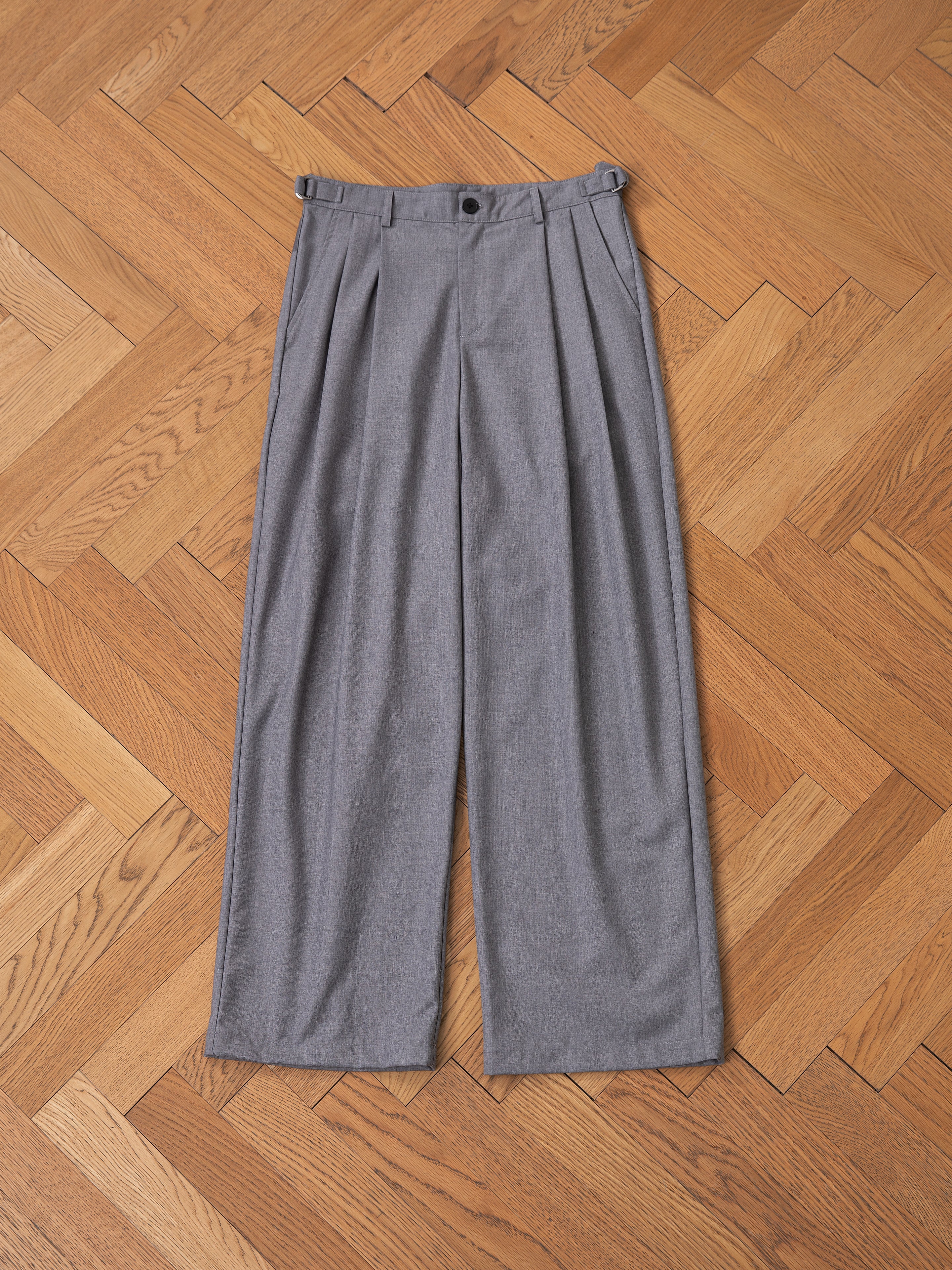 FOUND's Pleated Trousers in grey, featuring a relaxed fit, are stylishly displayed flat on a wooden parquet floor.