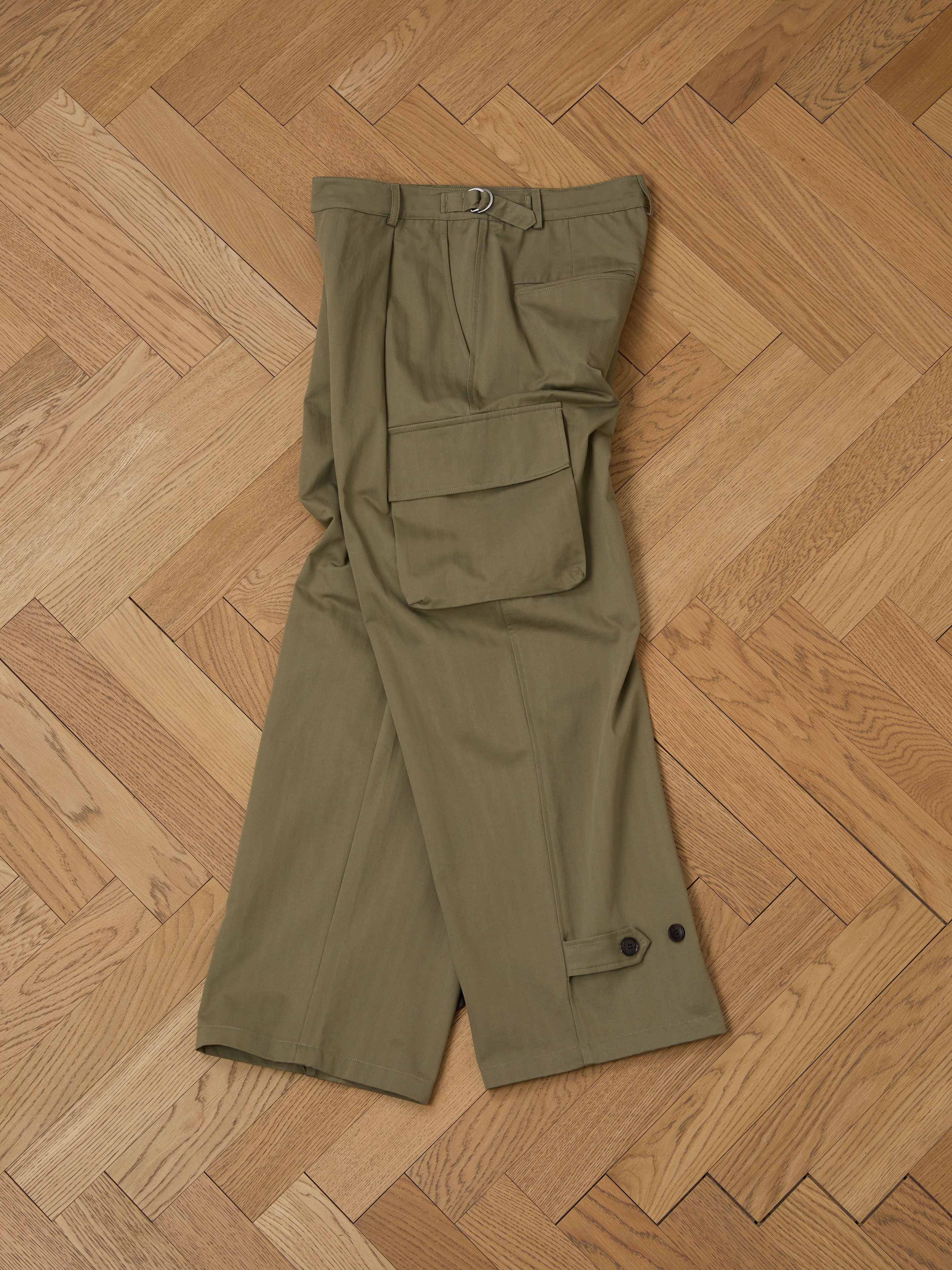 Olive green Hava Herringbone Pleated Cargo Trousers by FOUND, featuring side pockets, are laid flat on a wooden herringbone-patterned floor, showcasing chic utility wear.