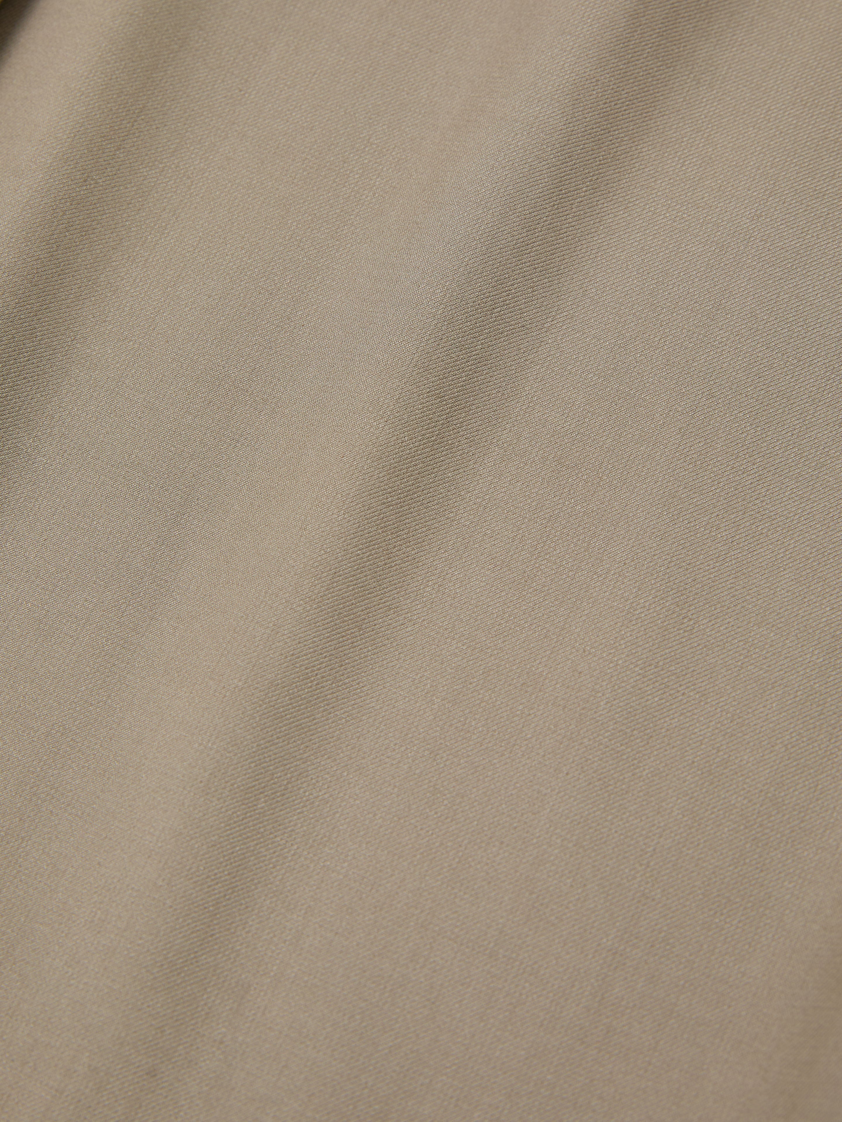 A close-up of the Hava Pleated Cargo Trousers by FOUND showcases beige textured cotton twill fabric with subtle diagonal lines, offering a hint of utilitarian style.