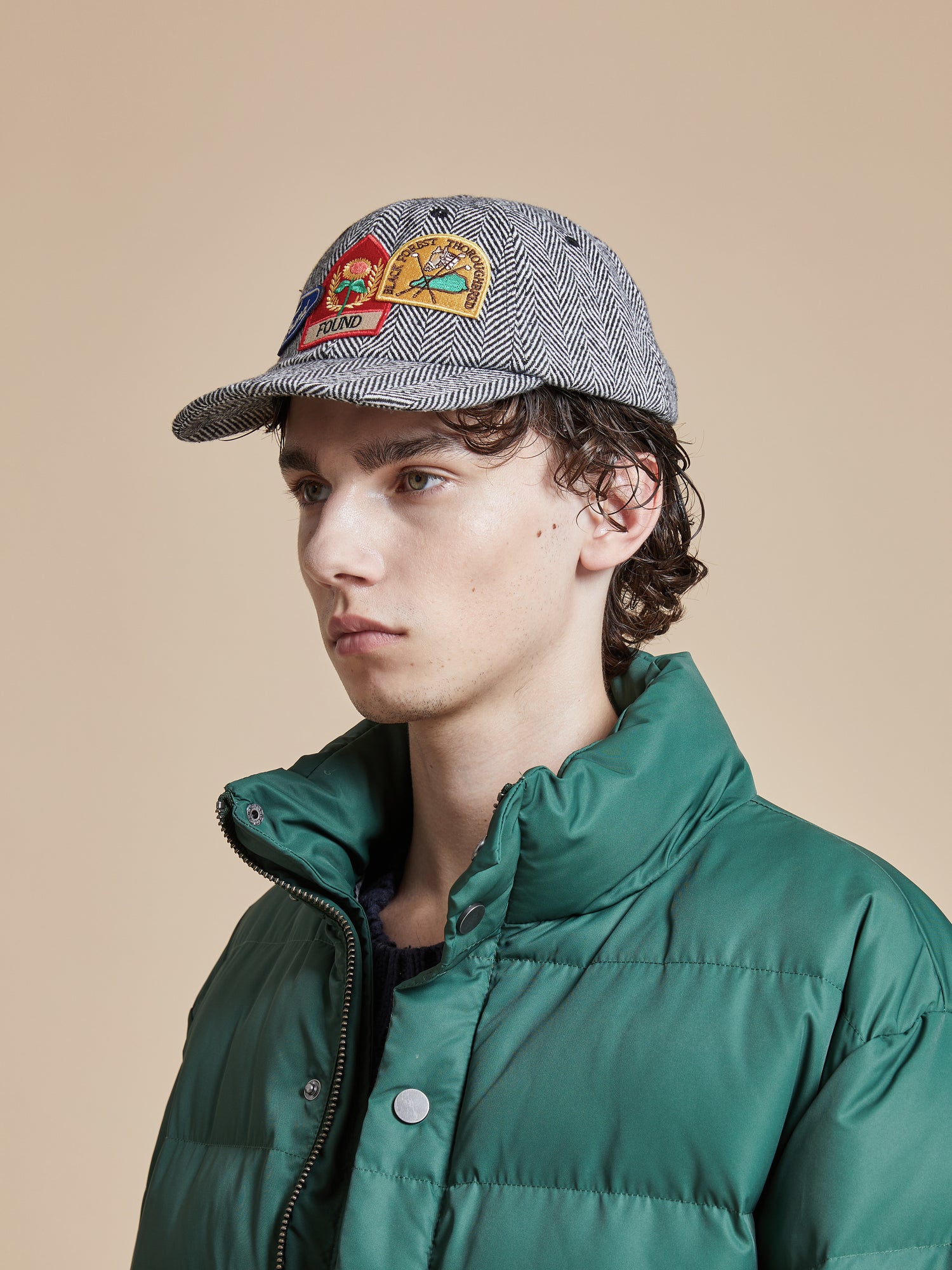 A young man wearing a green puffer jacket and a Found Herringbone Tweed Patch Cap.