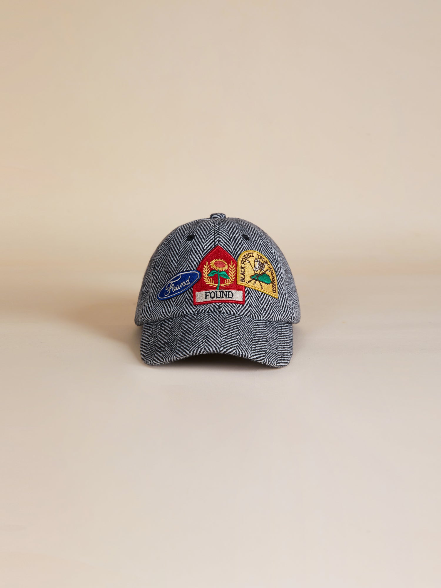 A Herringbone Tweed Patch Cap with a colorful embroidered Found logo on it.