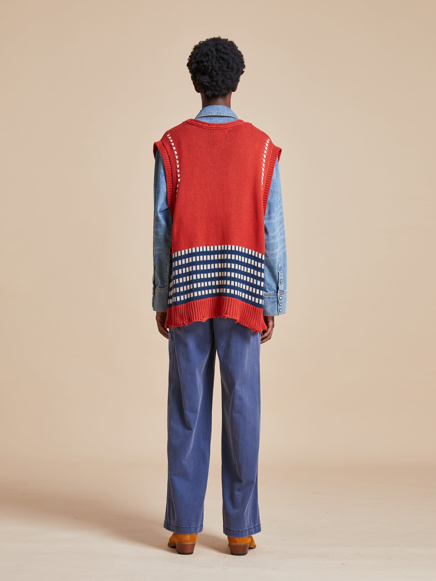 The back view of a man wearing a Found Homestead Check Sweater Knit Vest and blue pants.