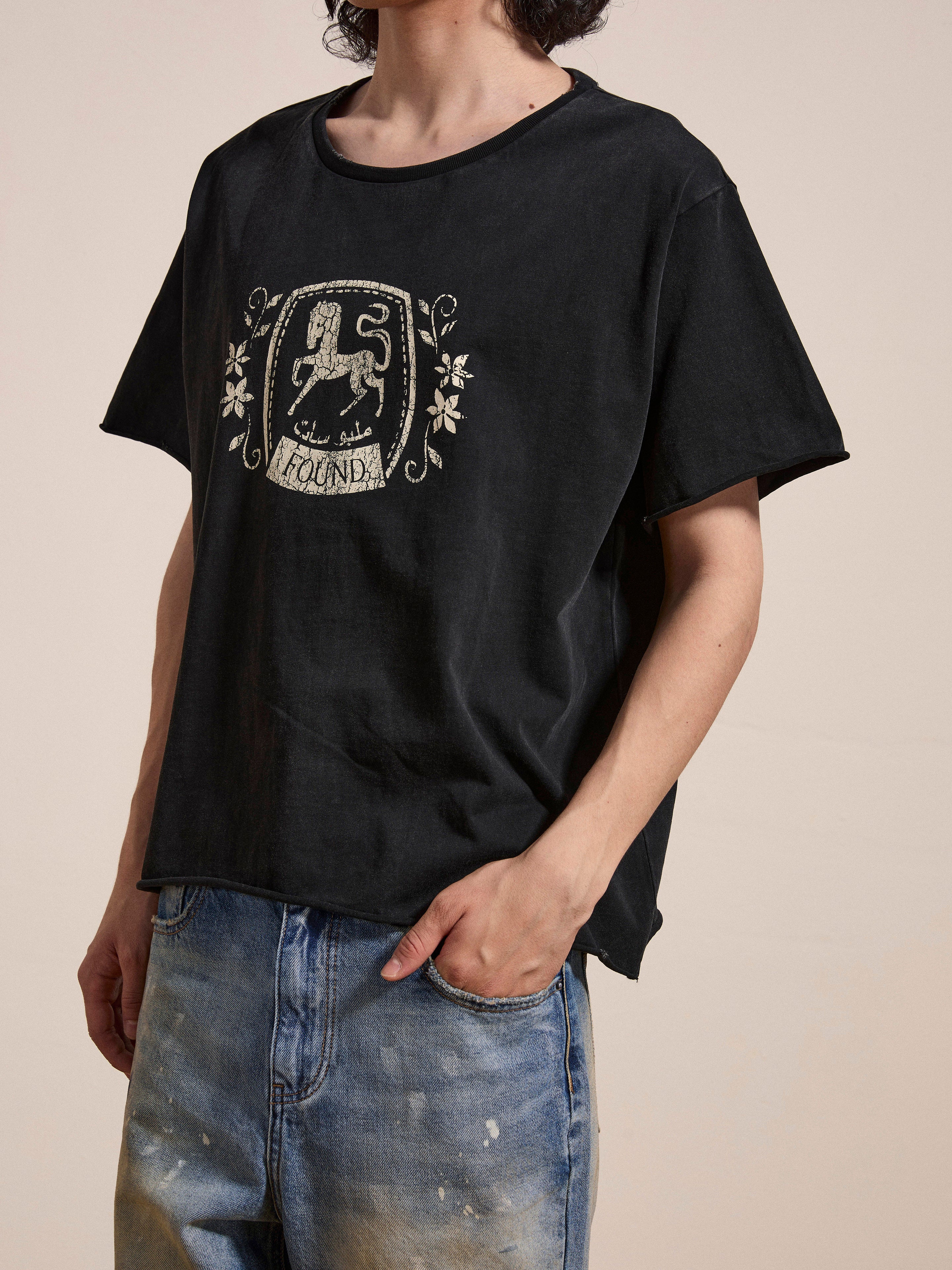 A person wearing a FOUND Horse Logo Print Tee made of 100% cotton with a graphic design and text, paired with enzyme wash faded blue jeans.