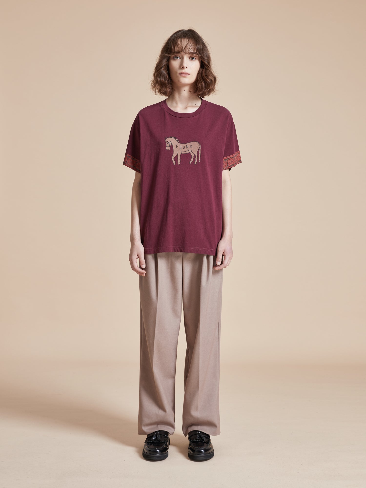 A woman wearing a Found Horse Embellishment Tee burgundy t-shirt and beige pants with floral motifs.