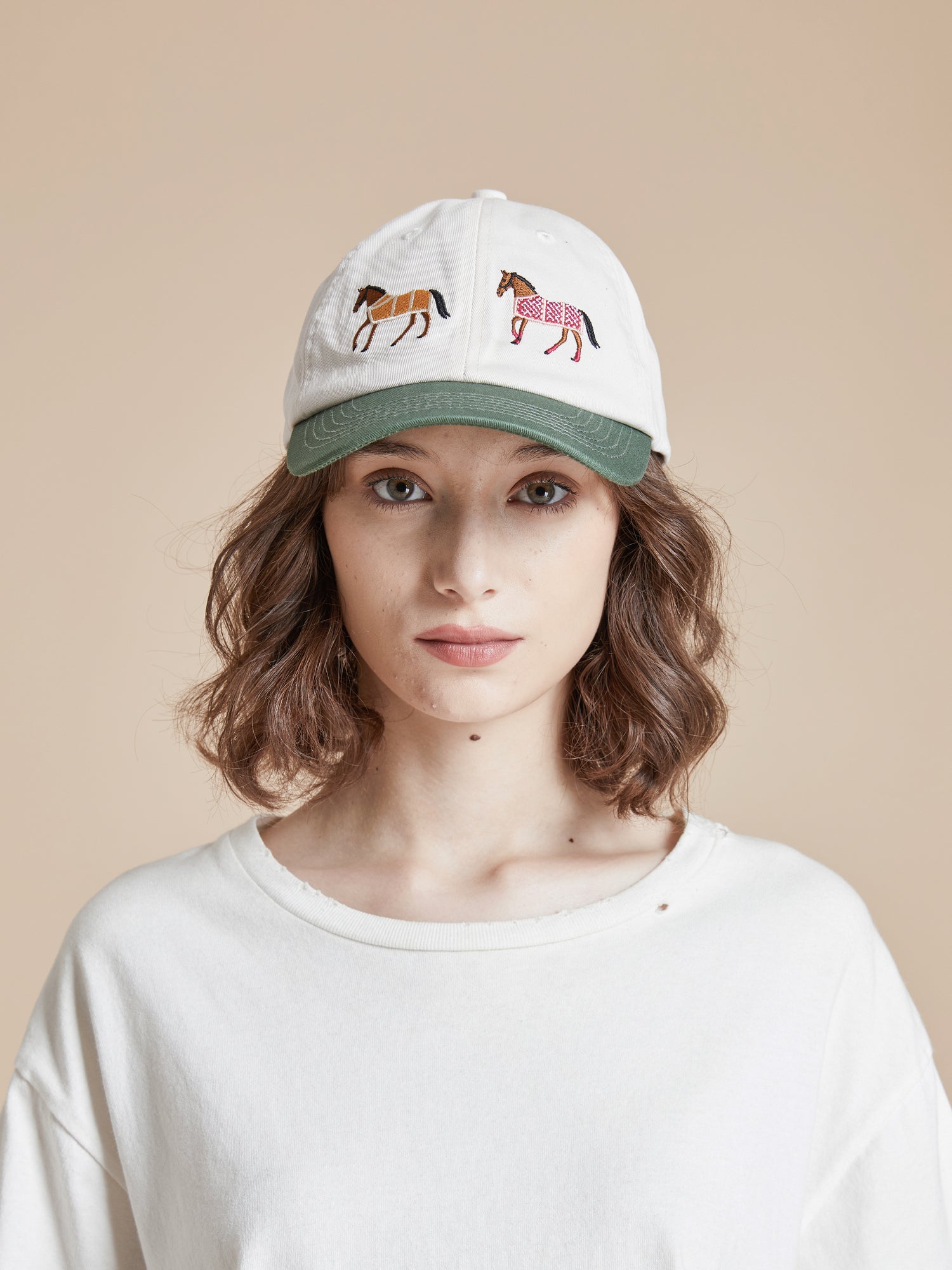 A woman wearing a white t-shirt with embroidered horses from the Found Horse Equine Cap brand on it.