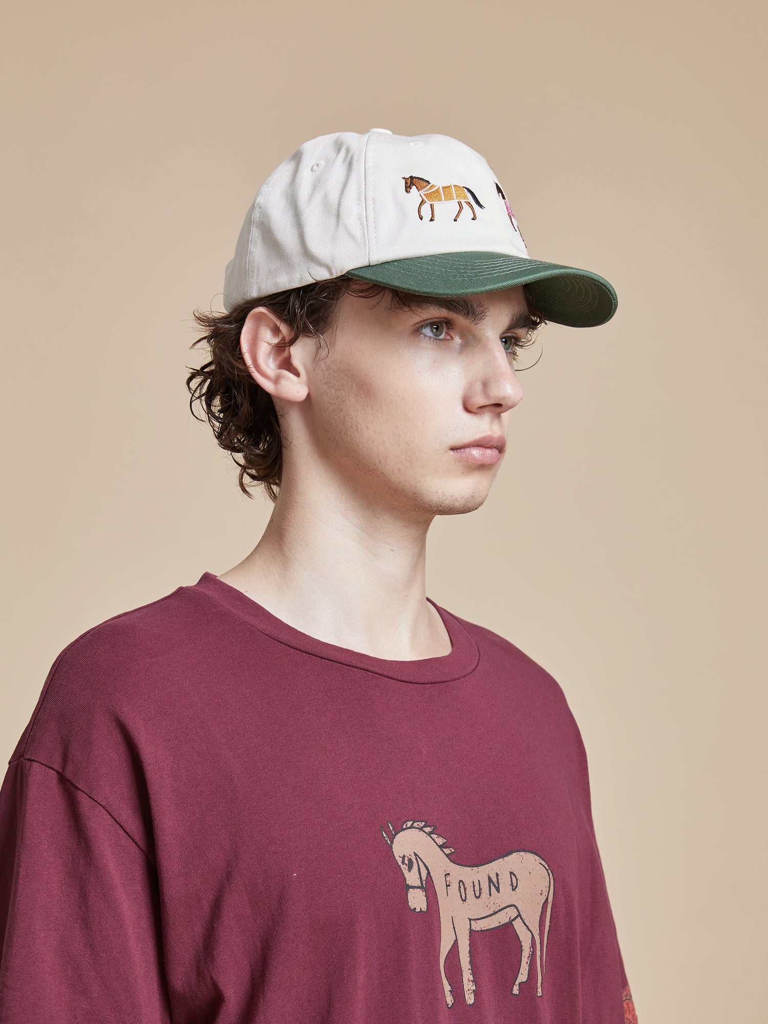 A man wearing a burgundy t-shirt with a Found Horse Equine Cap embroidered on it.