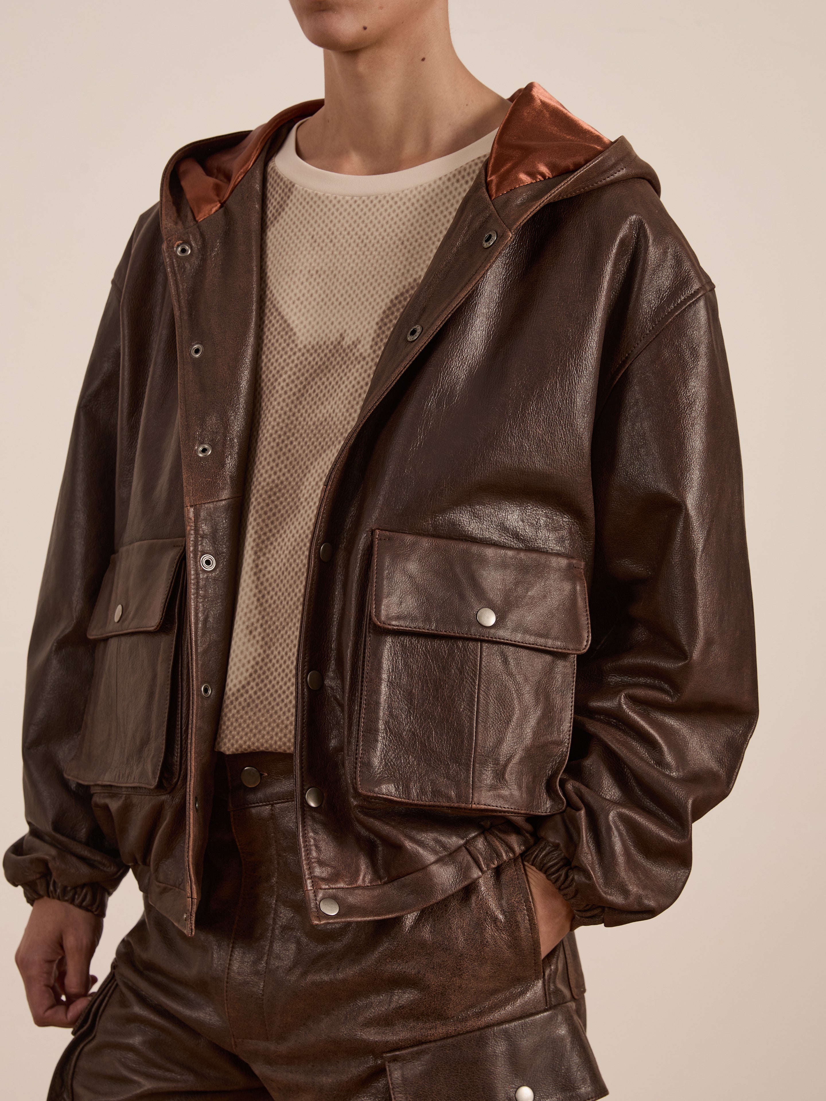 The person is wearing a dark brown leather jacket with large front pockets, exuding equestrian heritage, layered over FOUND's light beige Horse Racer Tee.