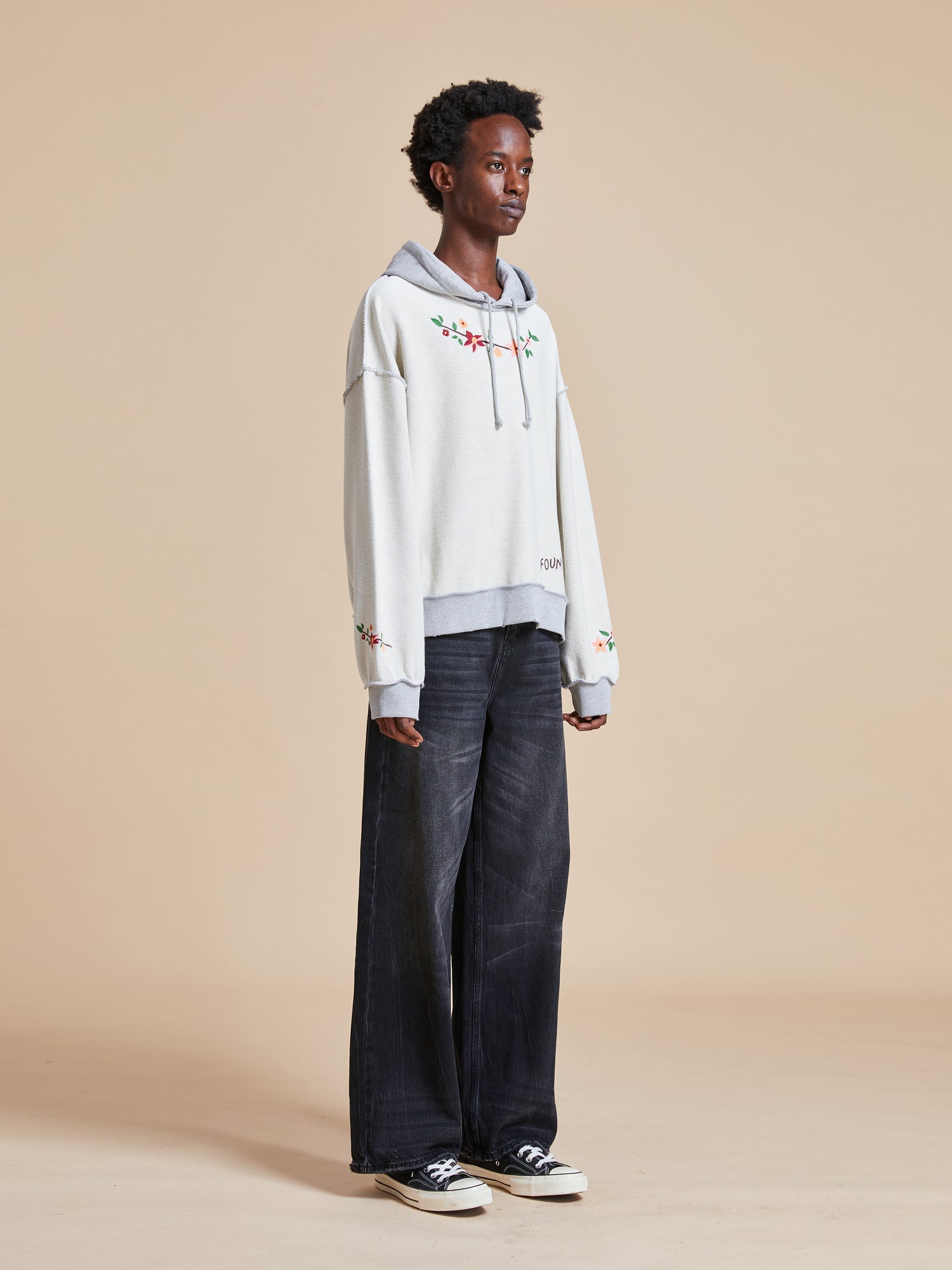 The model is wearing a white Inverse Flower Petal Hoodie and black wide leg pants.