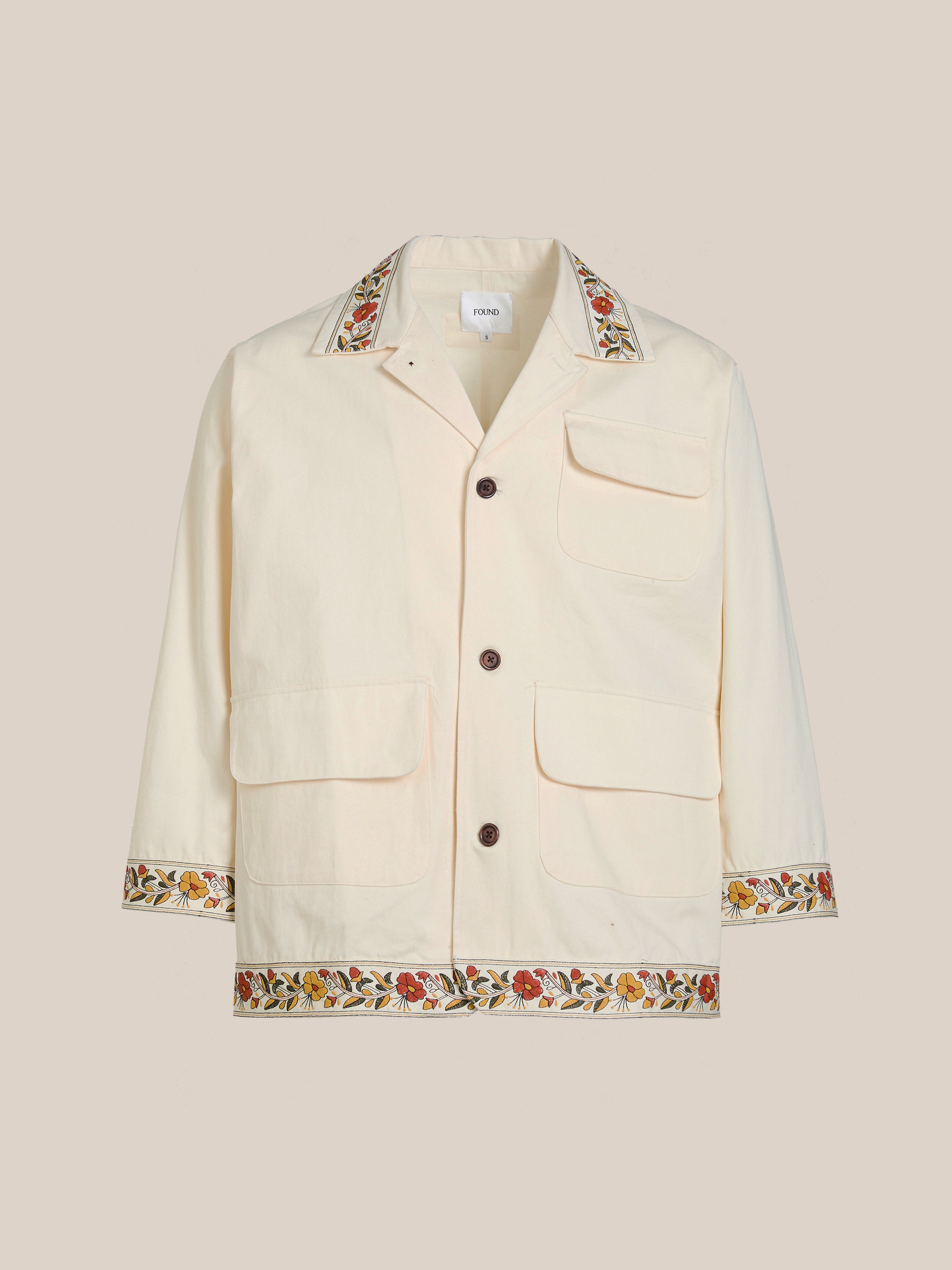 The Kantha Floral Work Jacket by FOUND is a beige piece that exudes vintage charm with exquisite Kantha floral embroidery on the collar, cuffs, and hem. It includes a stylish button closure and three functional front pockets, making it a versatile wardrobe staple.