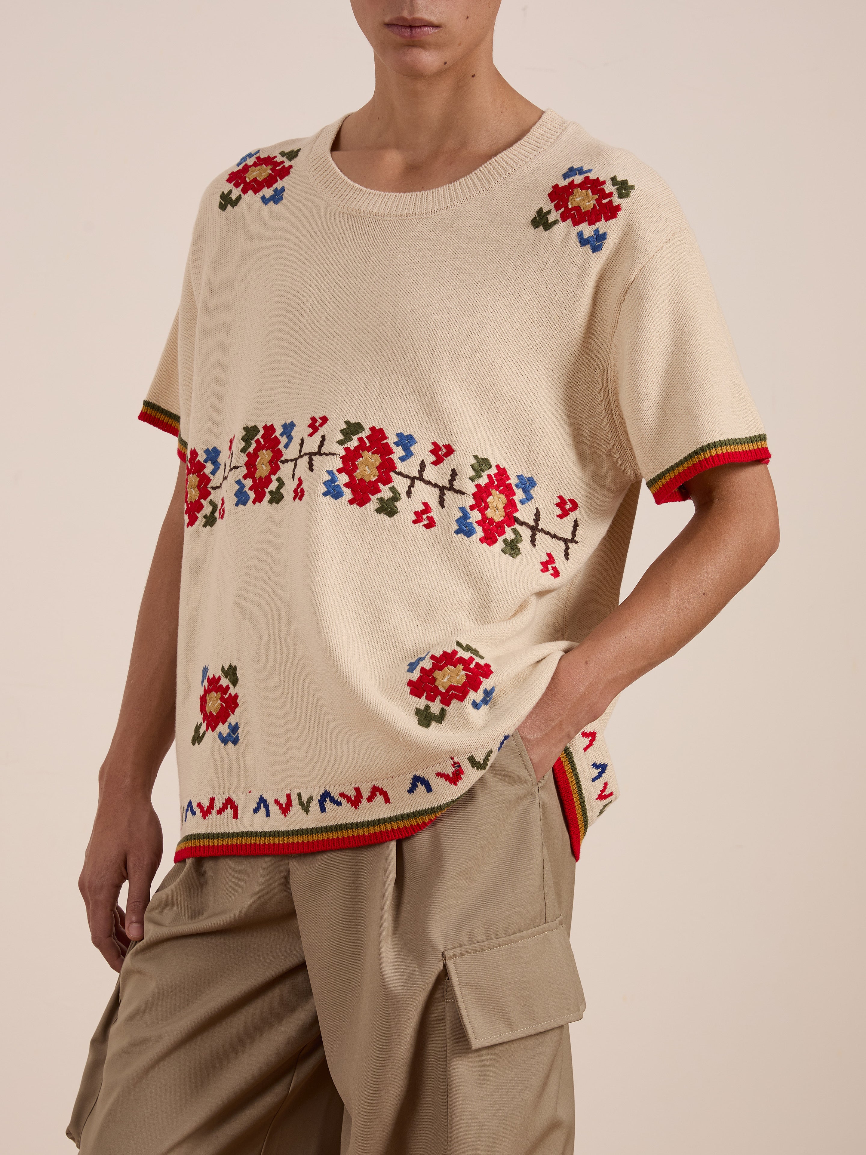 A person wears the Knit Flower Petal Tee by FOUND, a cream short-sleeve sweater adorned with jacquard floral motifs for a vintage-inspired charm, paired with beige cargo pants.