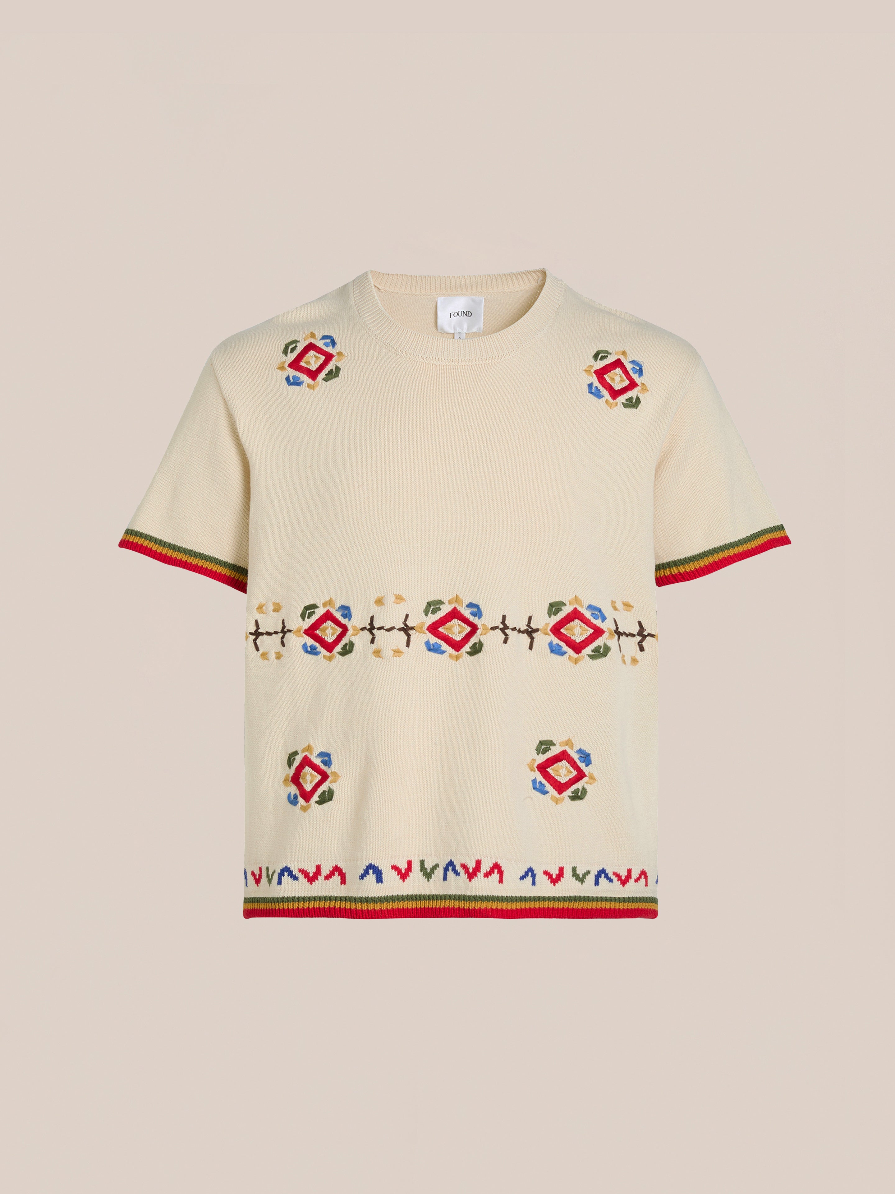 The Knit Flower Petal Tee by FOUND is a beige short-sleeve sweater featuring colorful geometric embroidery and red trim on the sleeves and hem, exuding vintage-inspired charm.