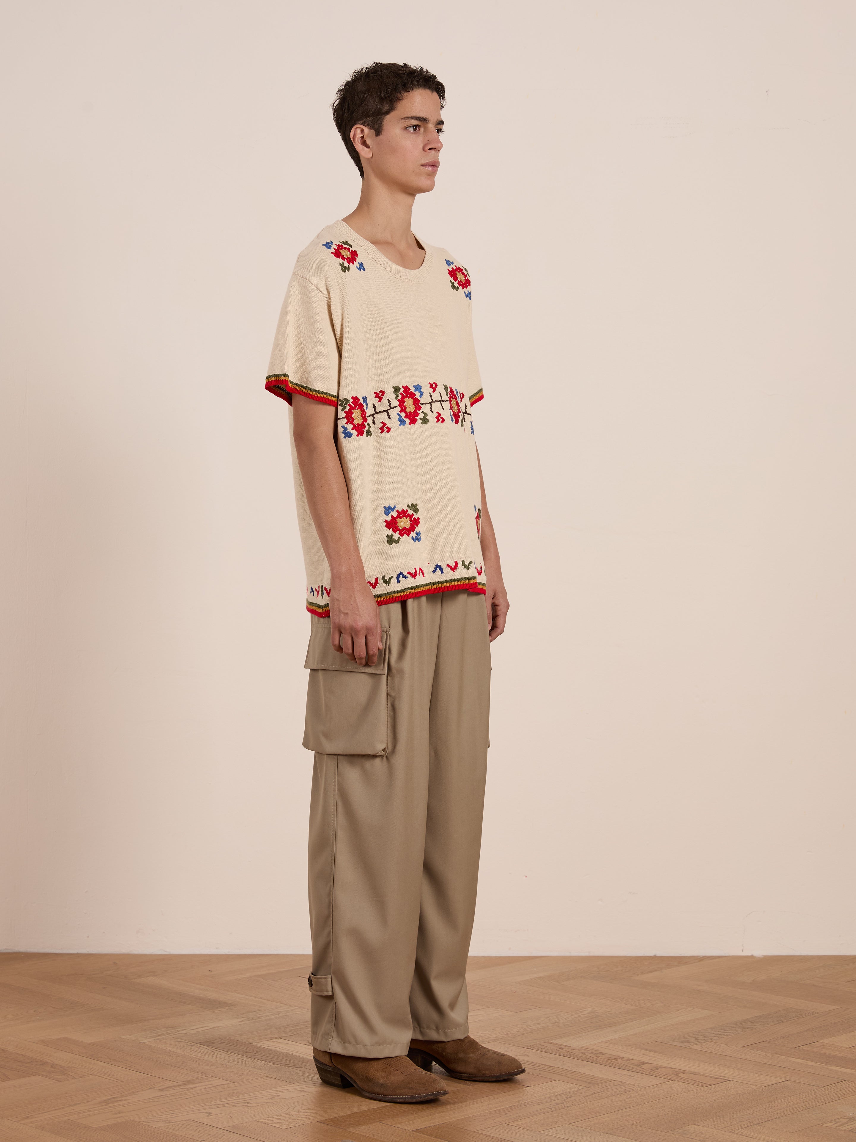 Standing on a wooden floor, the person wears the Knit Flower Petal Tee from FOUND, paired with khaki wide-leg cargo pants and brown shoes, projecting a vintage-inspired charm against a plain light background.