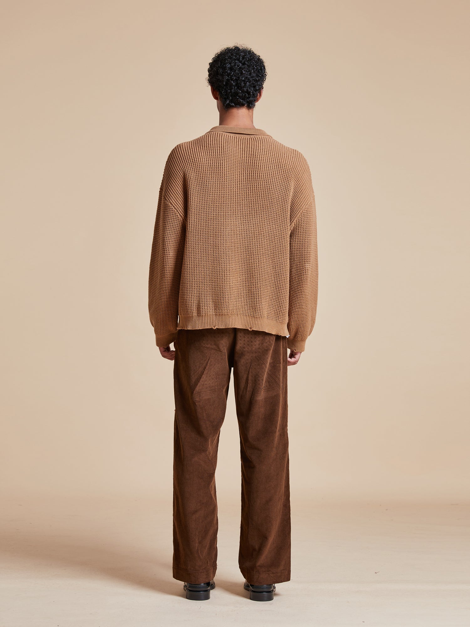 The back view of a man wearing a ginger-colored Found Tie-Collar Knit Sweater and corduroy pants, emanating a cozy feel.