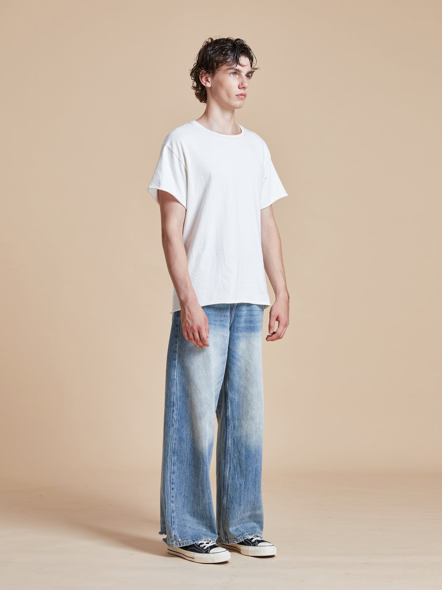 A man wearing a white t-shirt and Found Lacy Baggy Jeans Blue.