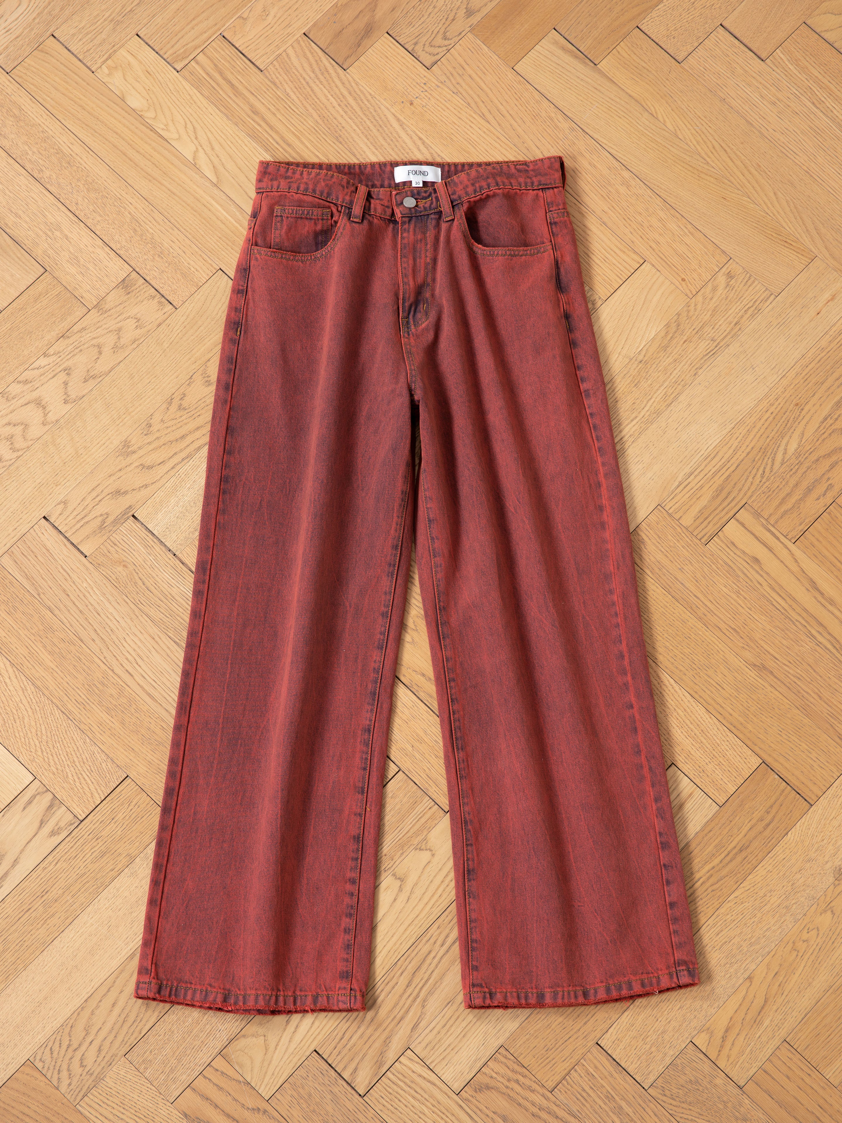 Lacy Baggy Jeans by FOUND, featuring a vintage red wash and wide-leg design with button and zipper fly, displayed on herringbone parquet flooring.