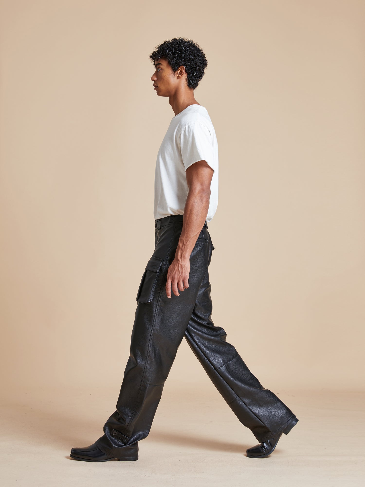 A man in Found faux leather cargo pants walking on a beige background.
