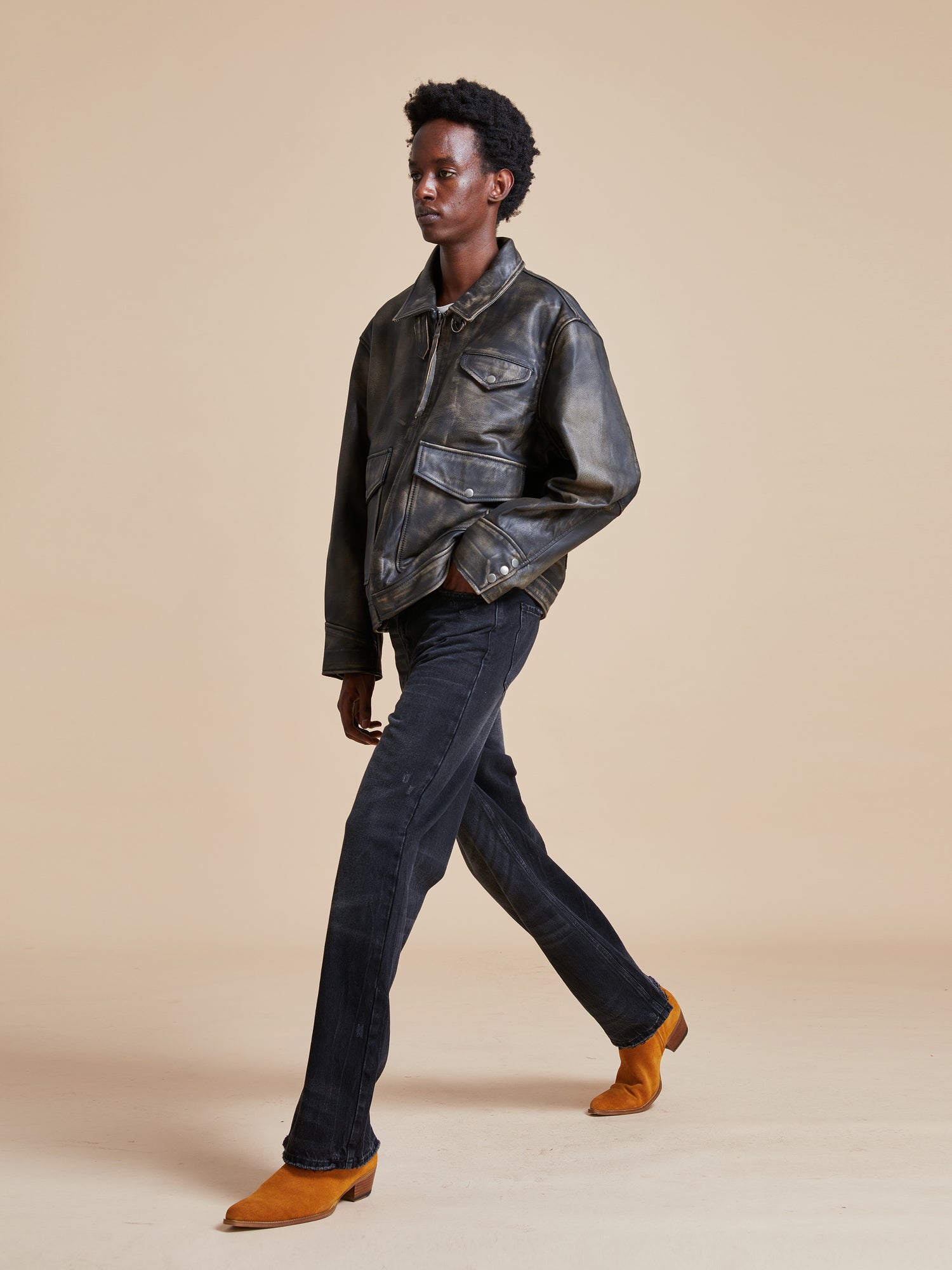 A man in a Found Distressed Leather Pocket Jacket and jeans walking on a beige background.