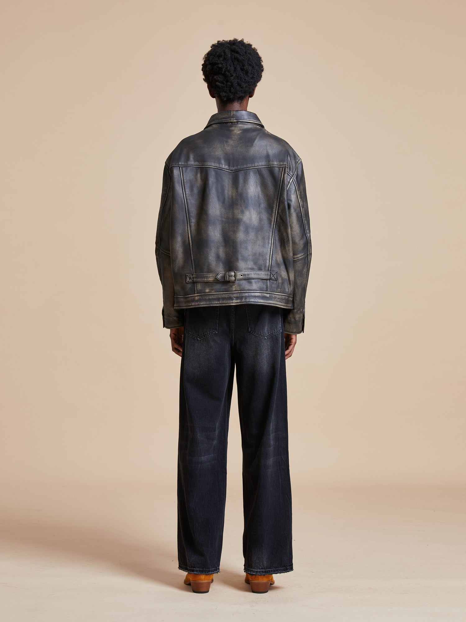 The back view of a man wearing a Found Distressed Leather Pocket Jacket and black pants.