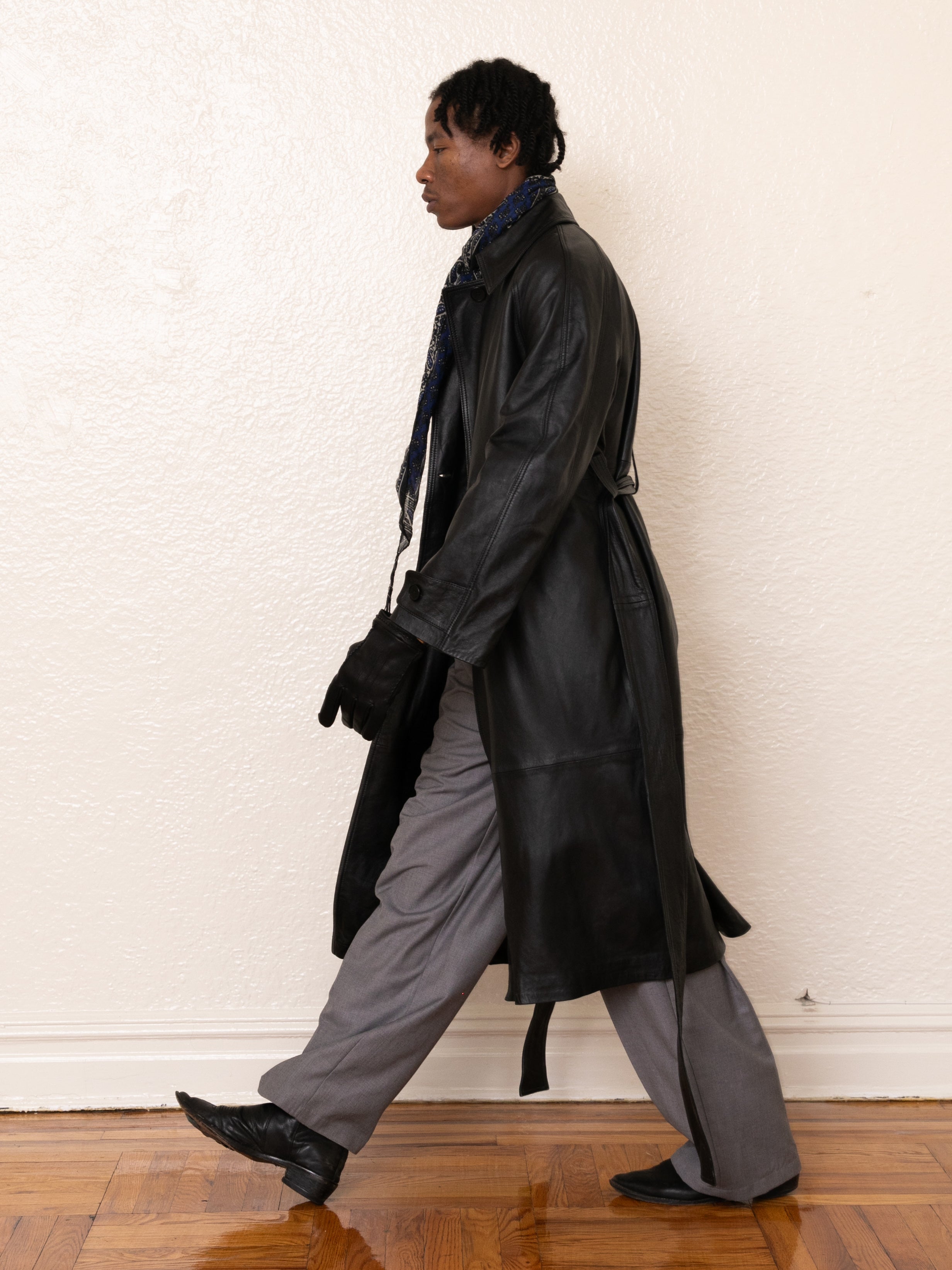 A person in an ethically crafted FOUND Leather Trench Coat, made of lightweight cowhide, walks left in gray pants against a plain background.