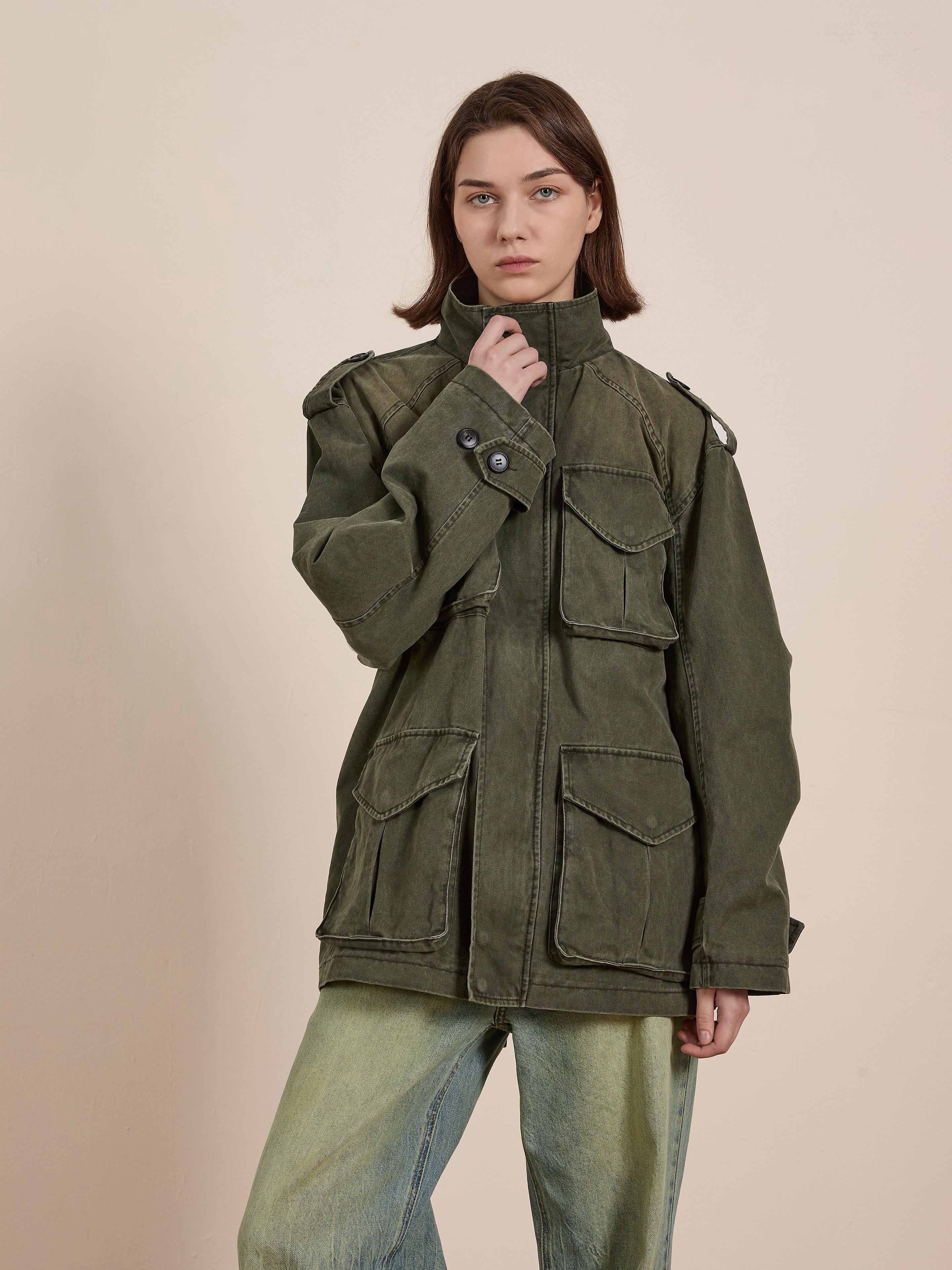 Wearing FOUND's green M65 Utility Twill Pocket Jacket with light jeans, a person models a vintage look against a plain backdrop.