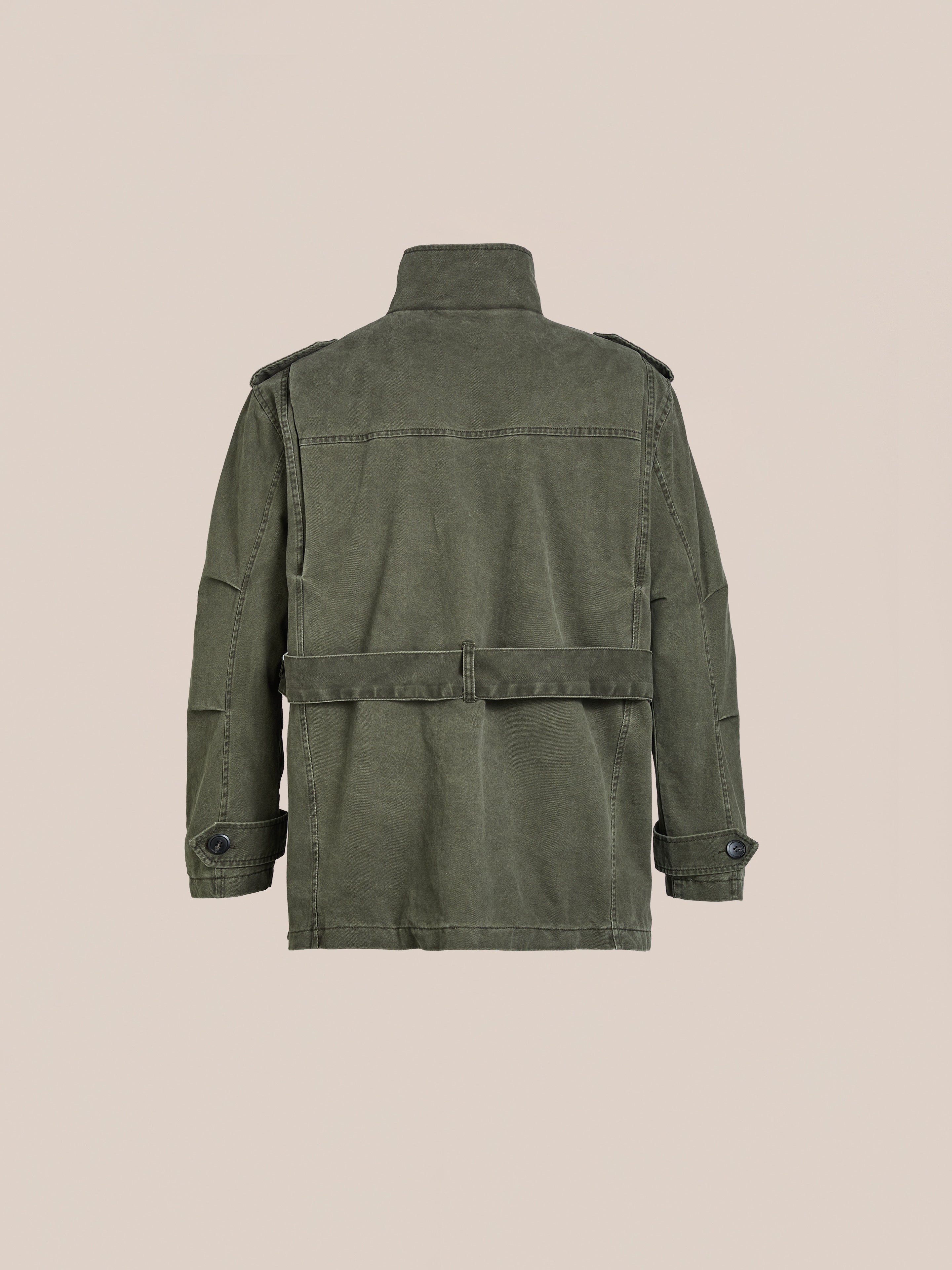 An olive green FOUND M65 Utility Twill Pocket Jacket with buttoned cuffs and shoulder epaulettes is showcased on a beige backdrop. This unisex relaxed-fit design captures classic military-inspired style.