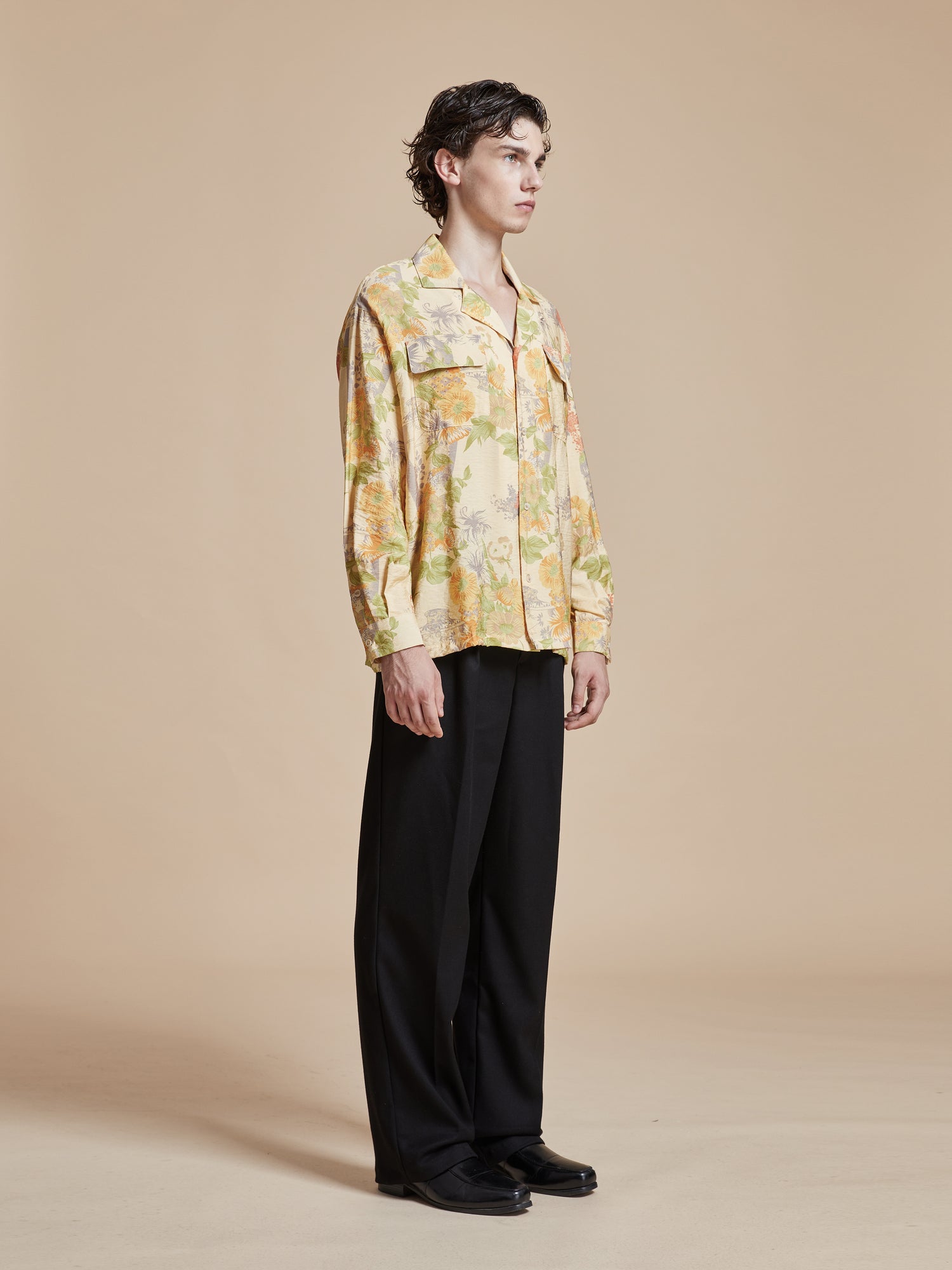 A model wearing a yellow floral shirt with nature-inspired Phulkari motifs, the Meraj Vase Pot Long Sleeve Camp Shirt from Found, and black trousers.