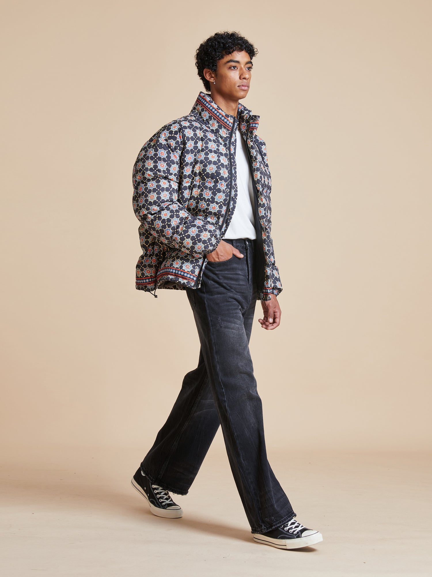 A man in a patterned Found Ajrak Block Puffer Jacket walking on a beige background.