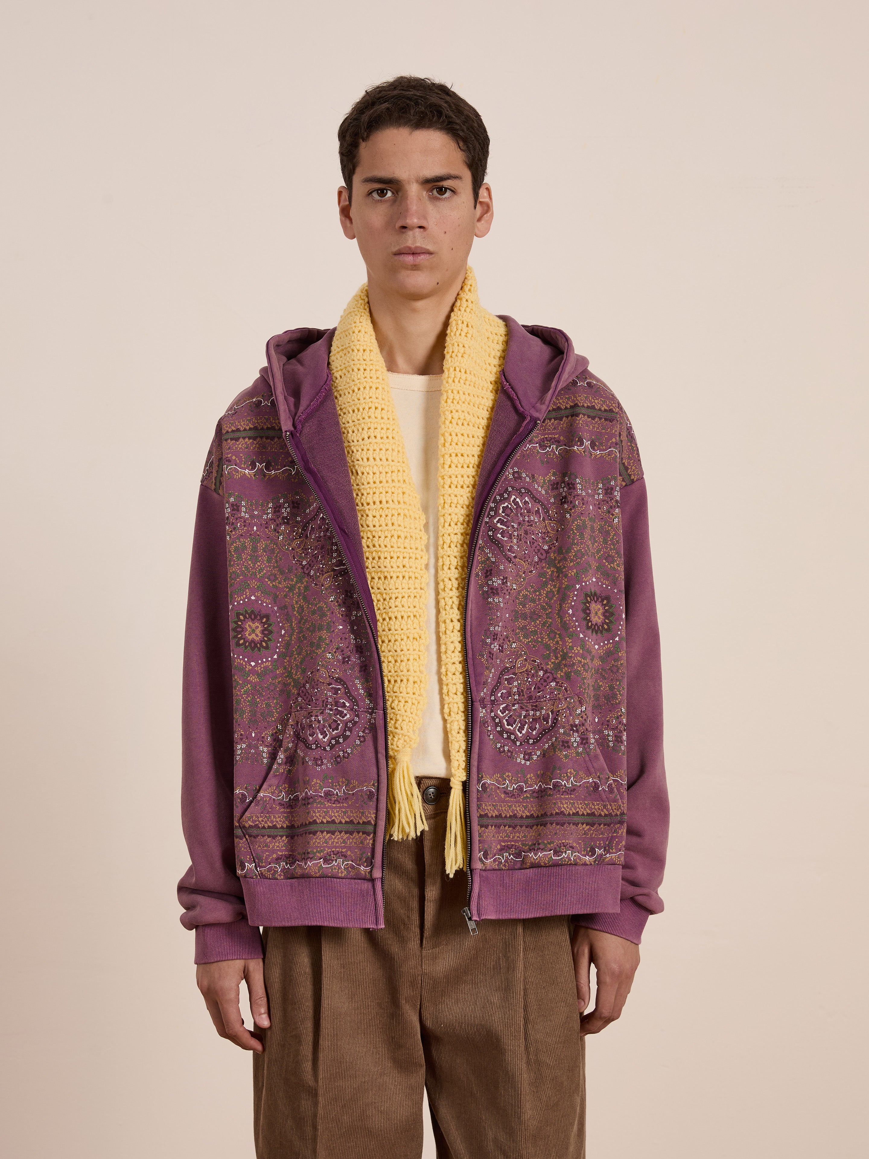 Someone highlights their streetwear essential: the FOUND Motif Zip-Up Hoodie in a purple mandala pattern, styled with a yellow scarf and brown pants, set against a plain background.