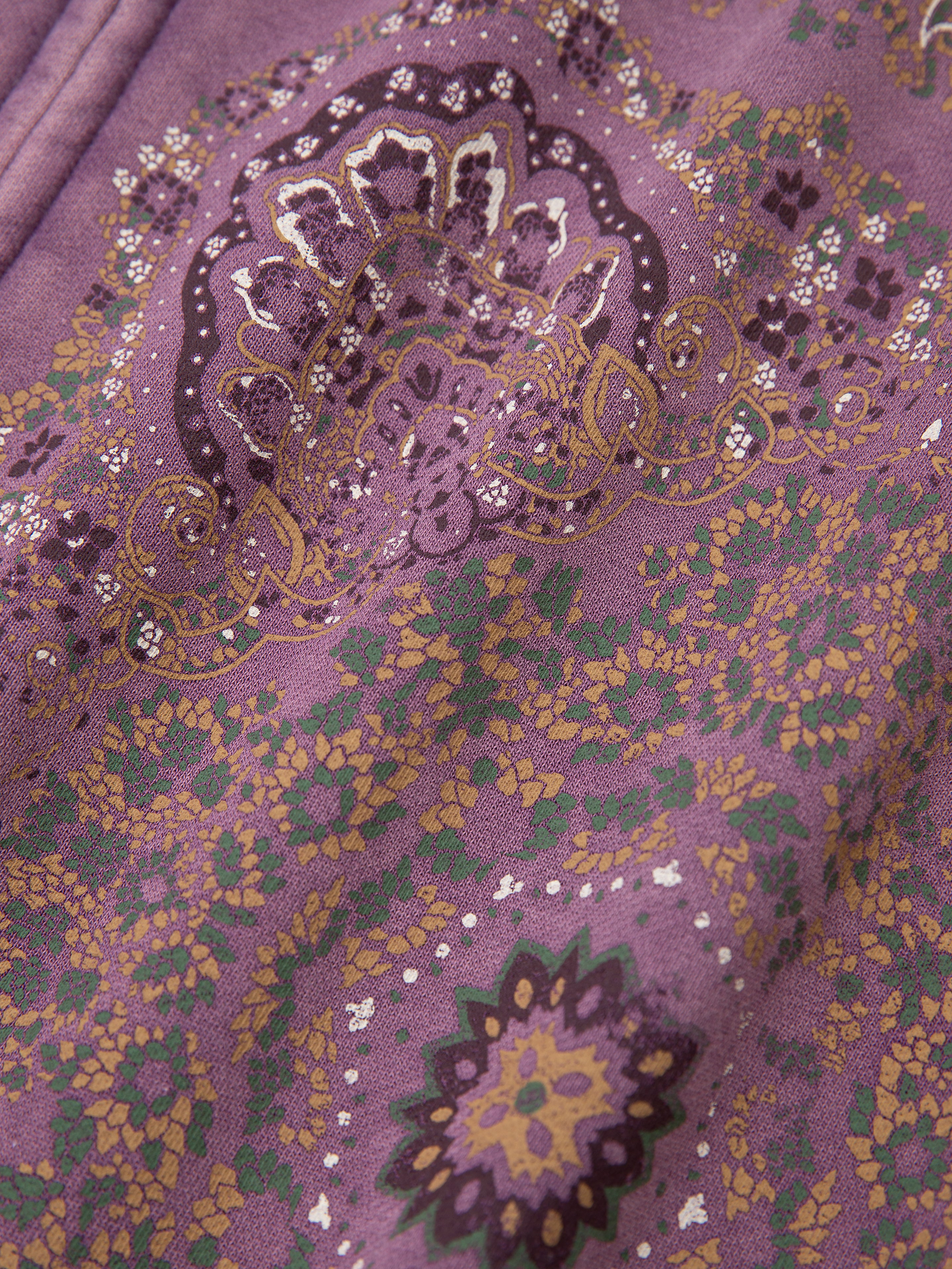 The Motif Zip-Up Hoodie by FOUND features a close-up of purple fabric with an intricate floral and geometric mandala art pattern, accented in gold, green, and white.