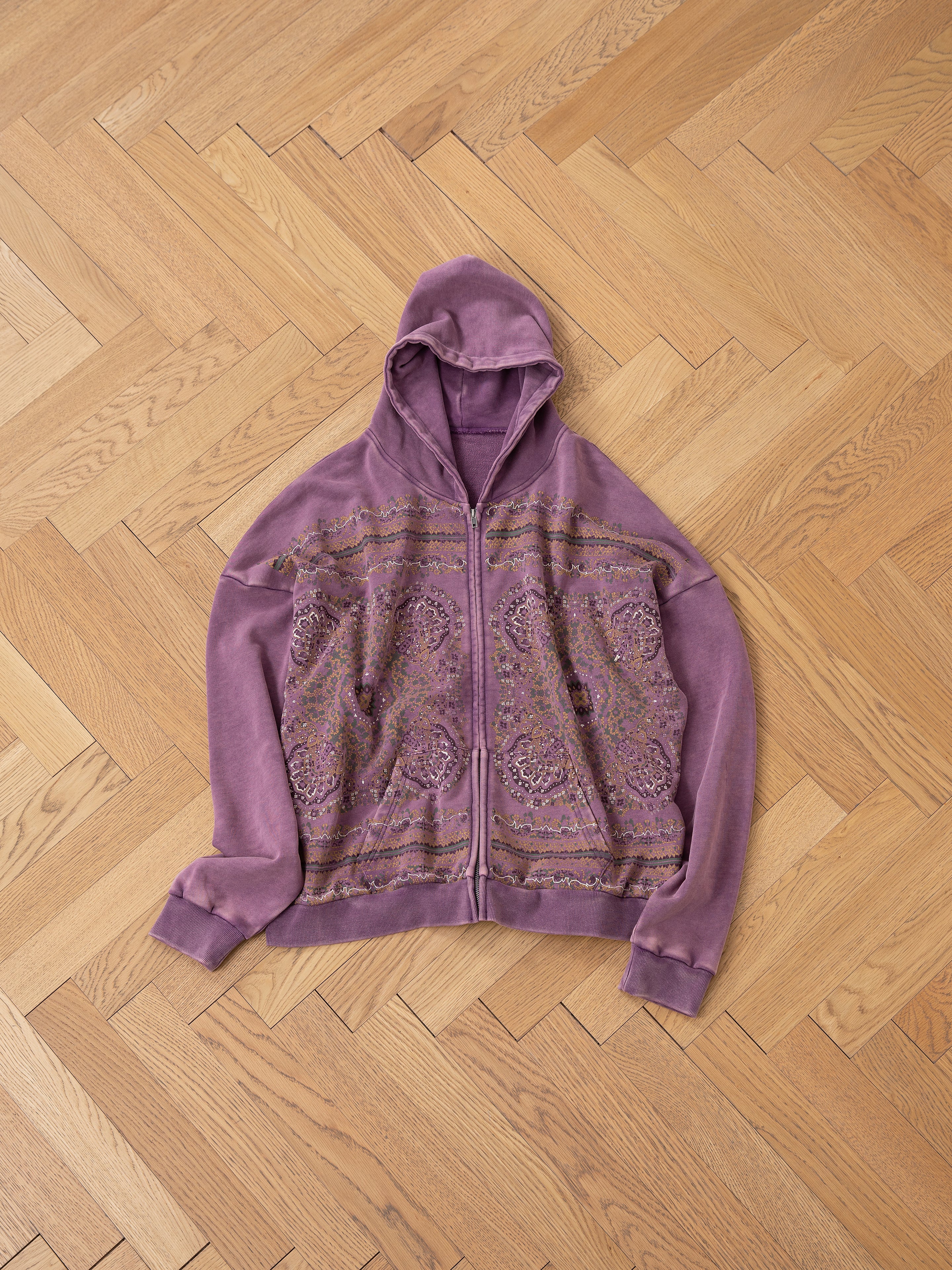 The FOUND Motif Zip-Up Hoodie, featuring intricate mandala art, is laid flat on a wooden herringbone floor—an essential piece for streetwear enthusiasts.