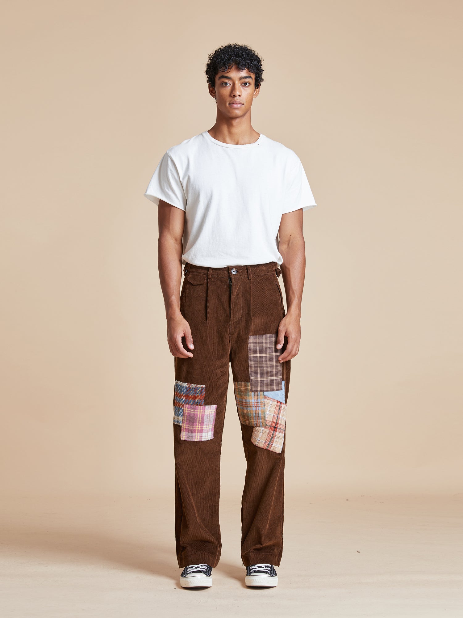 A man wearing Found Multi-Plaid Patch Corduroy Pants with fabric patches.