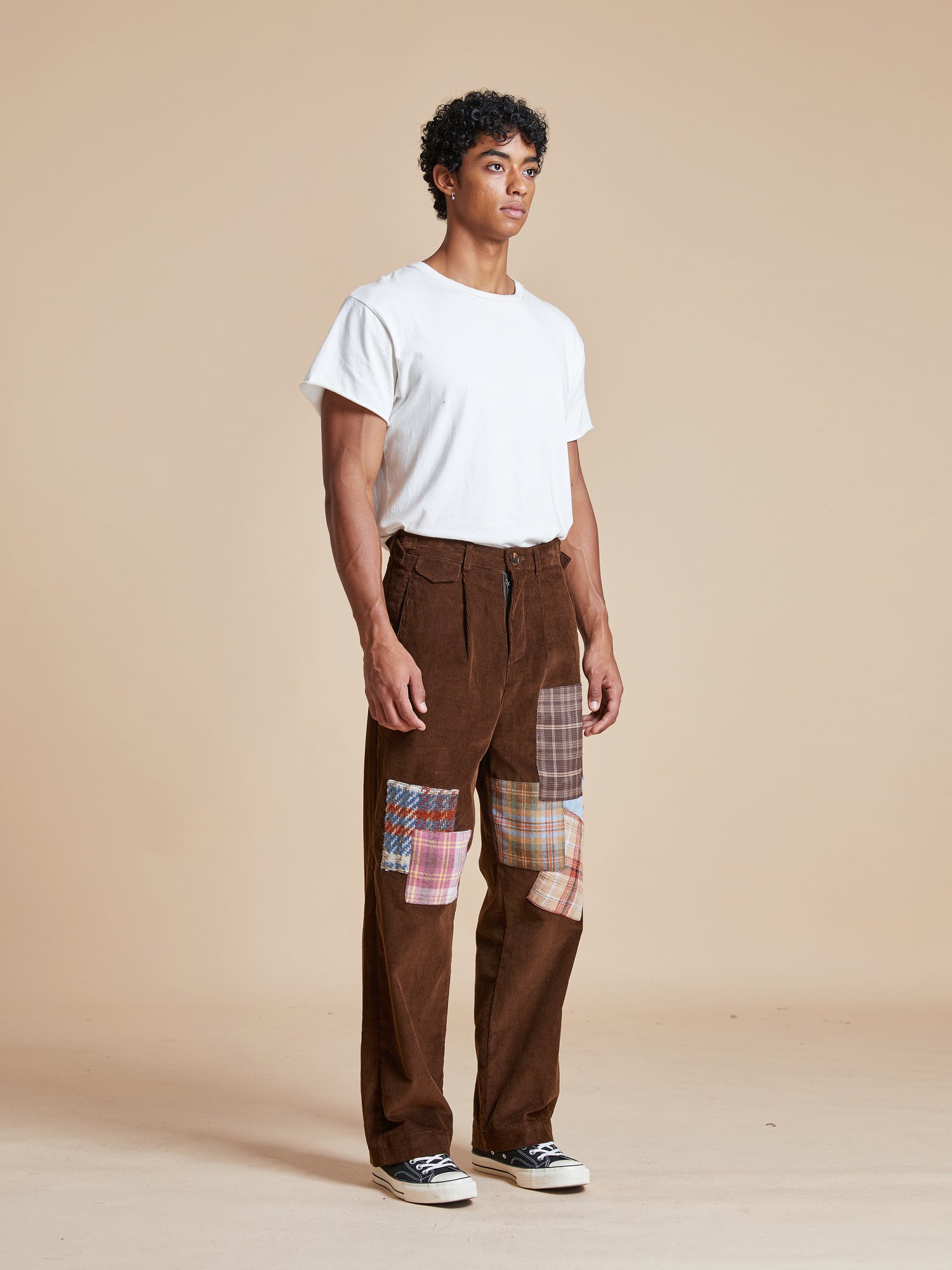 A man wearing Multi-Plaid Patch Corduroy Pants by Found with fabric patches.