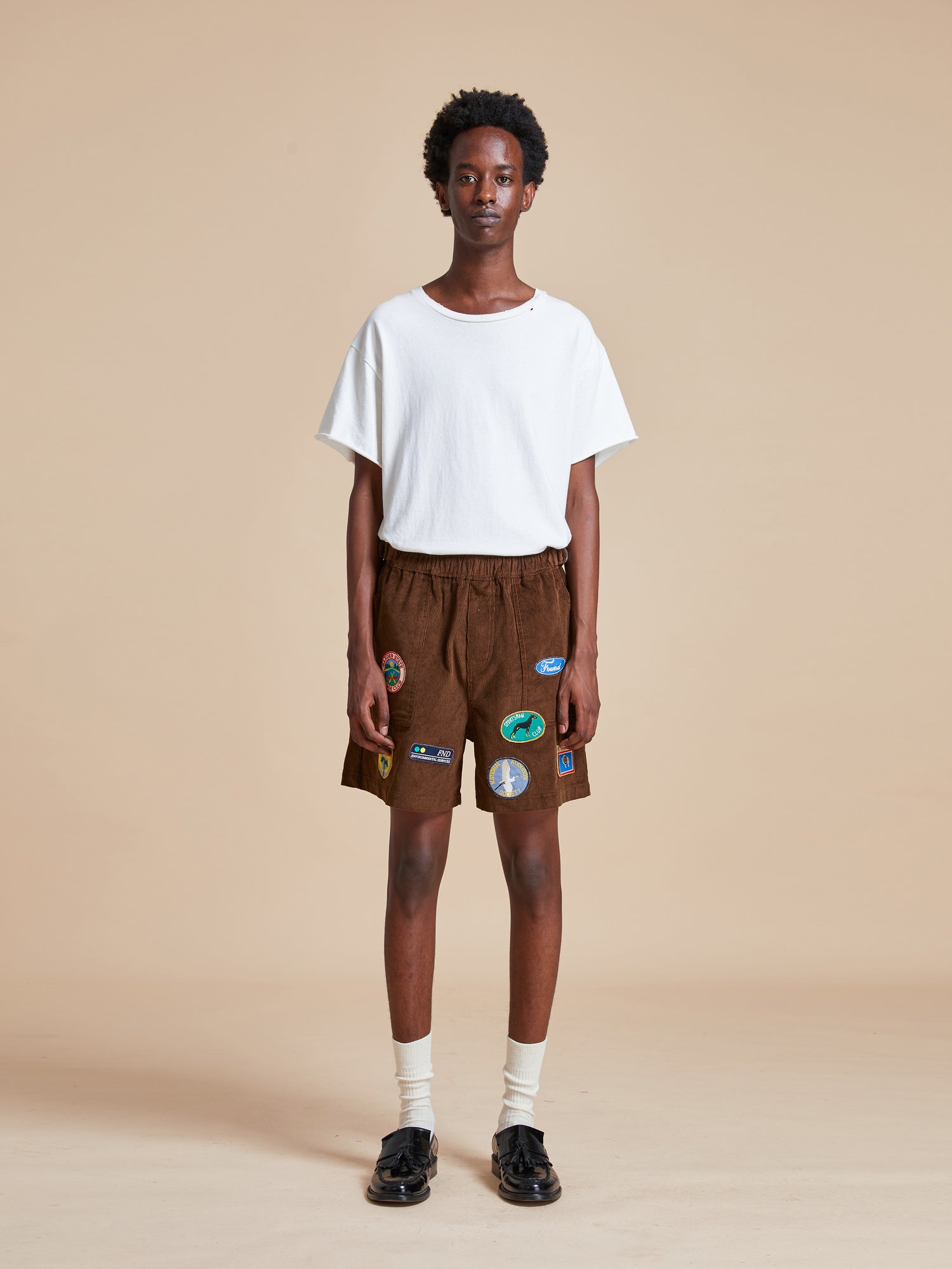 The model is wearing a white t-shirt and Found Canoe Multi Patch Corduroy Shorts.