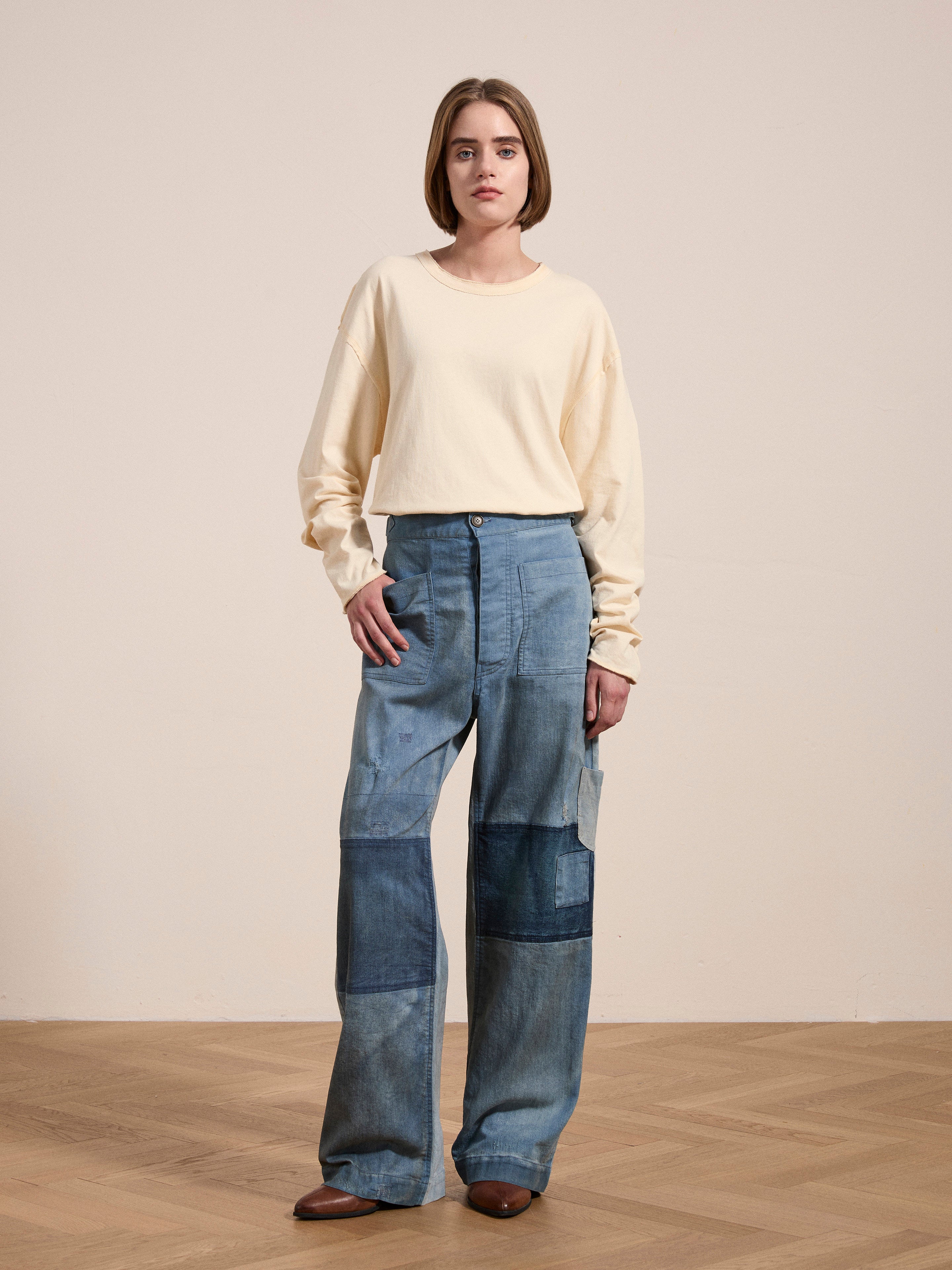 A person standing on a wooden floor wearing a beige long-sleeved shirt and blue FOUND Multi Patch Painters Work Pants for that classic slouchy fit.