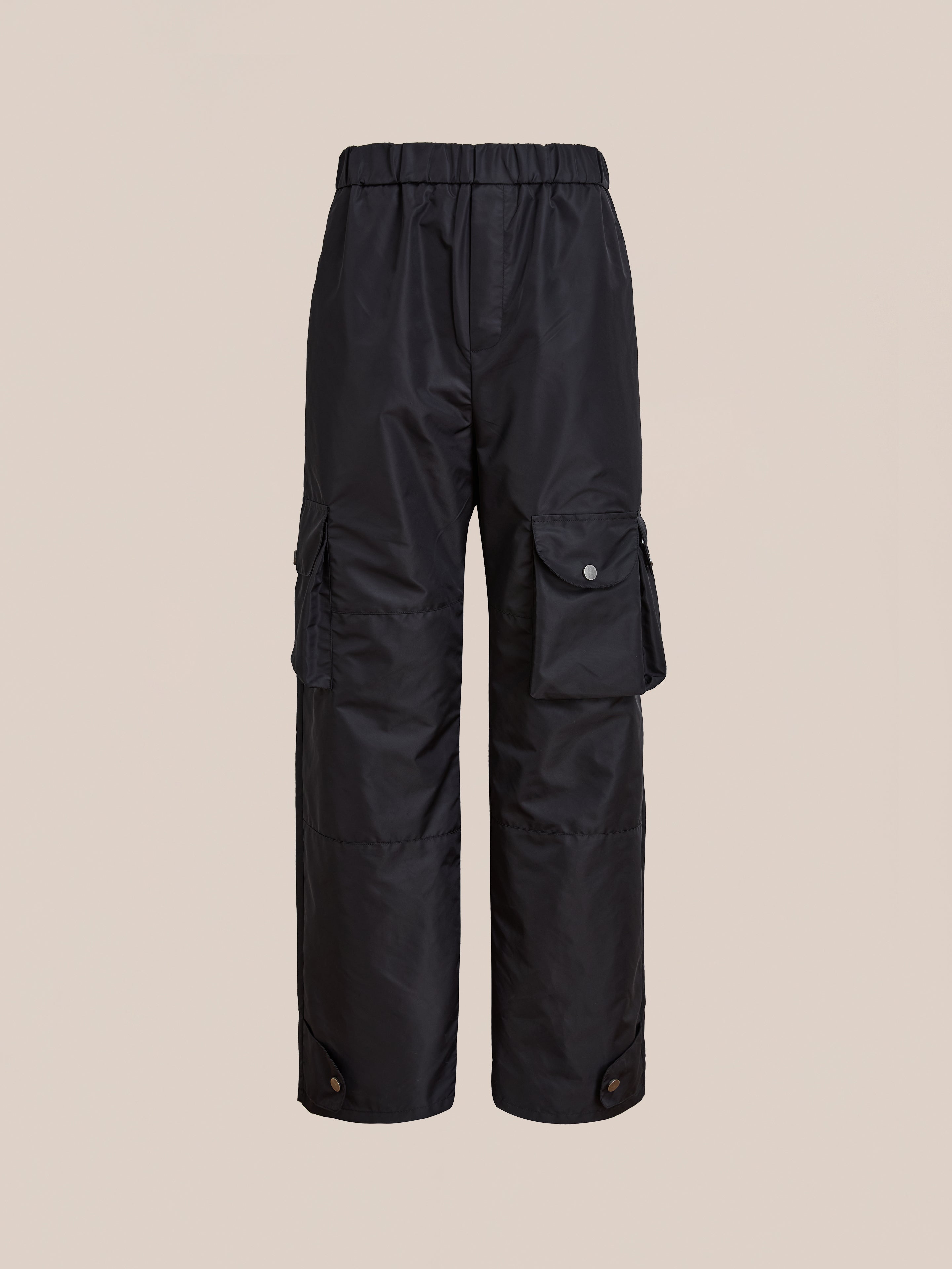 FOUND Nylon Cargo Pants: Unisex black relaxed-fit nylon pants with elastic waistband, side flap pockets, buttoned cuffs, and multiple pockets. Shown on a plain beige background.