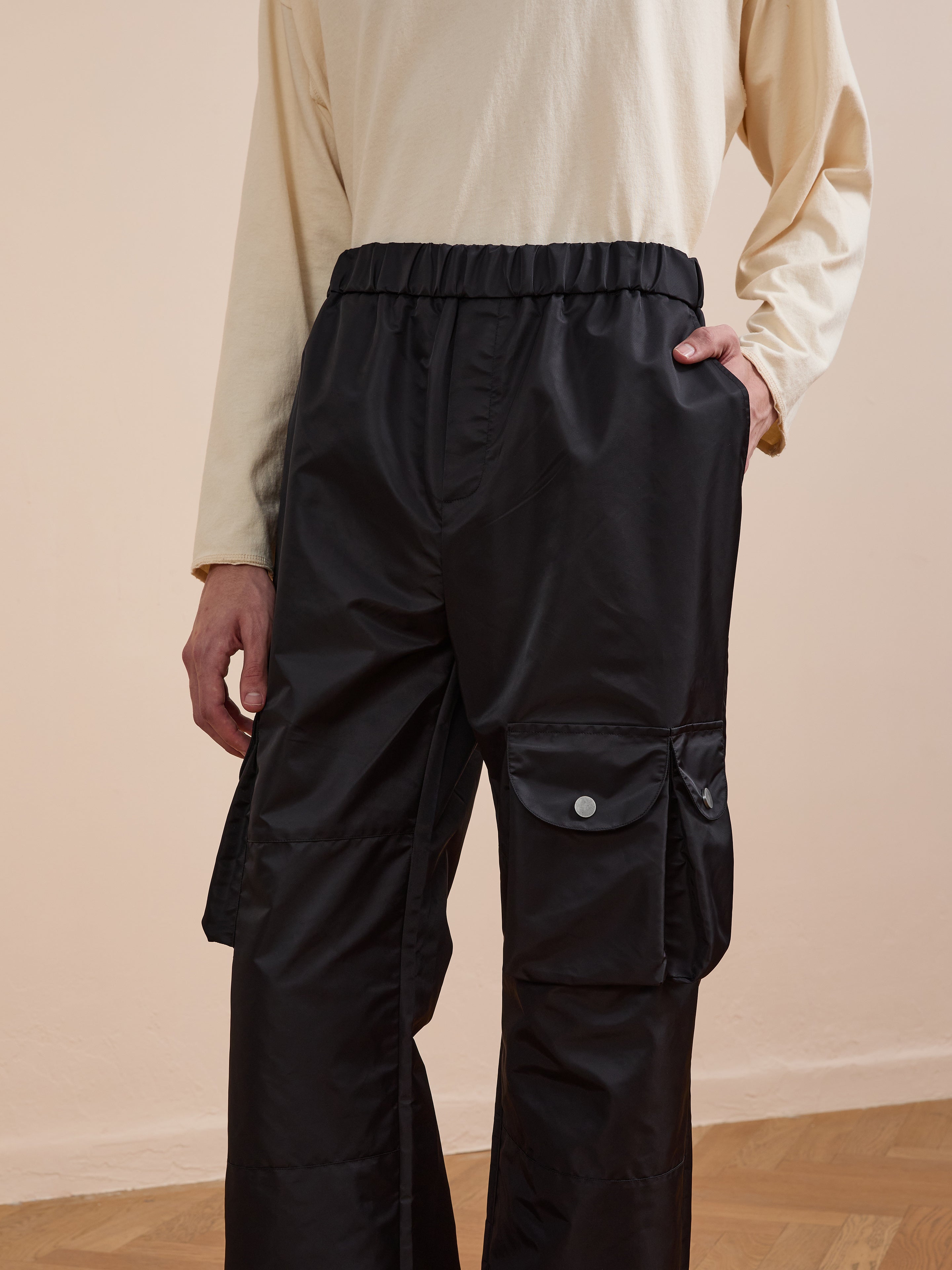 A person in FOUND Nylon Cargo Pants with a relaxed fit and long-sleeved beige shirt stands against a neutral background, one hand in their pocket.